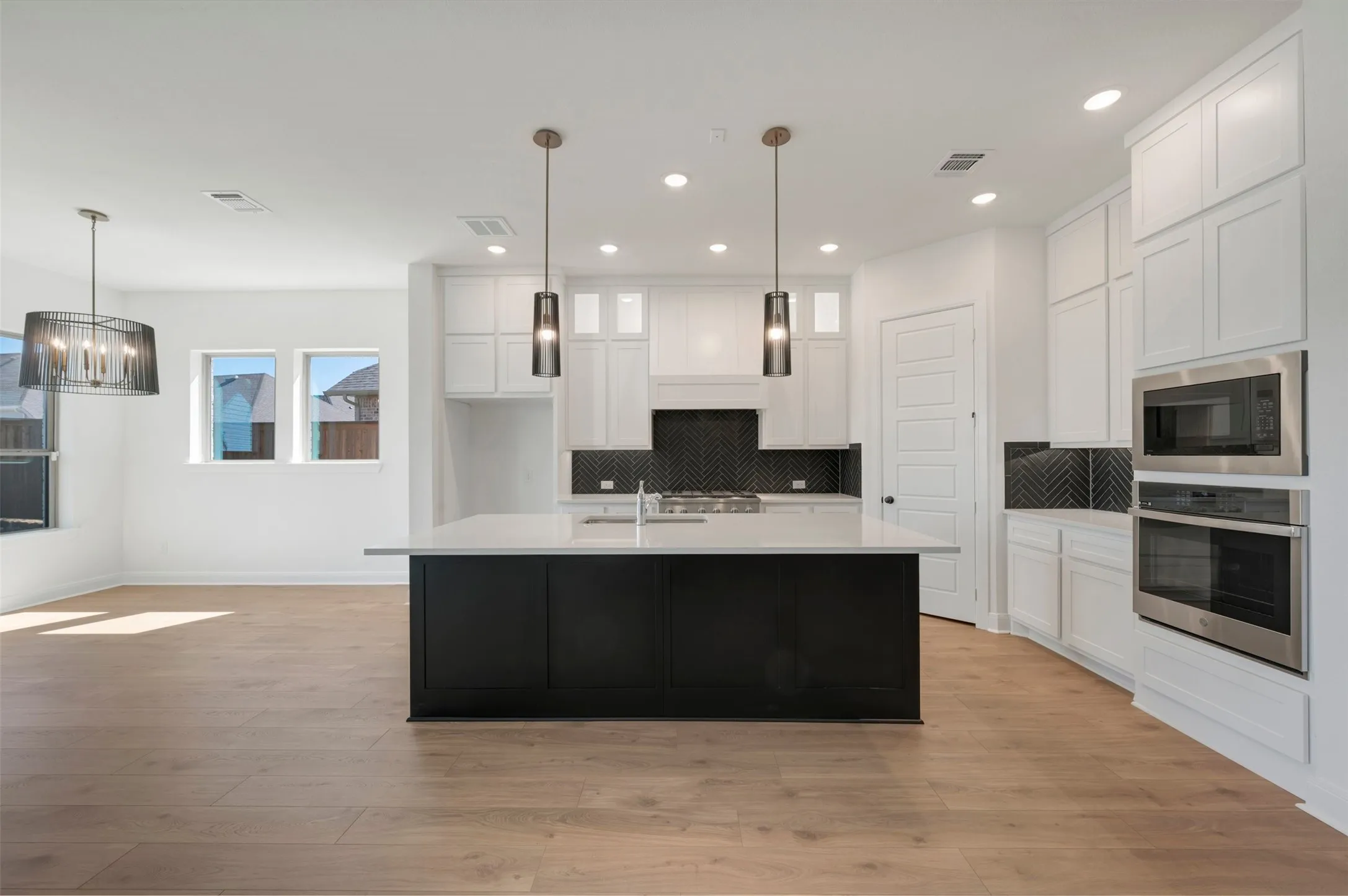 Open-concept kitchen featuring an island with a white countertop, white cabinetry, a herringbone pattern backsplash, stainless steel appliances, and wood-finish flooring