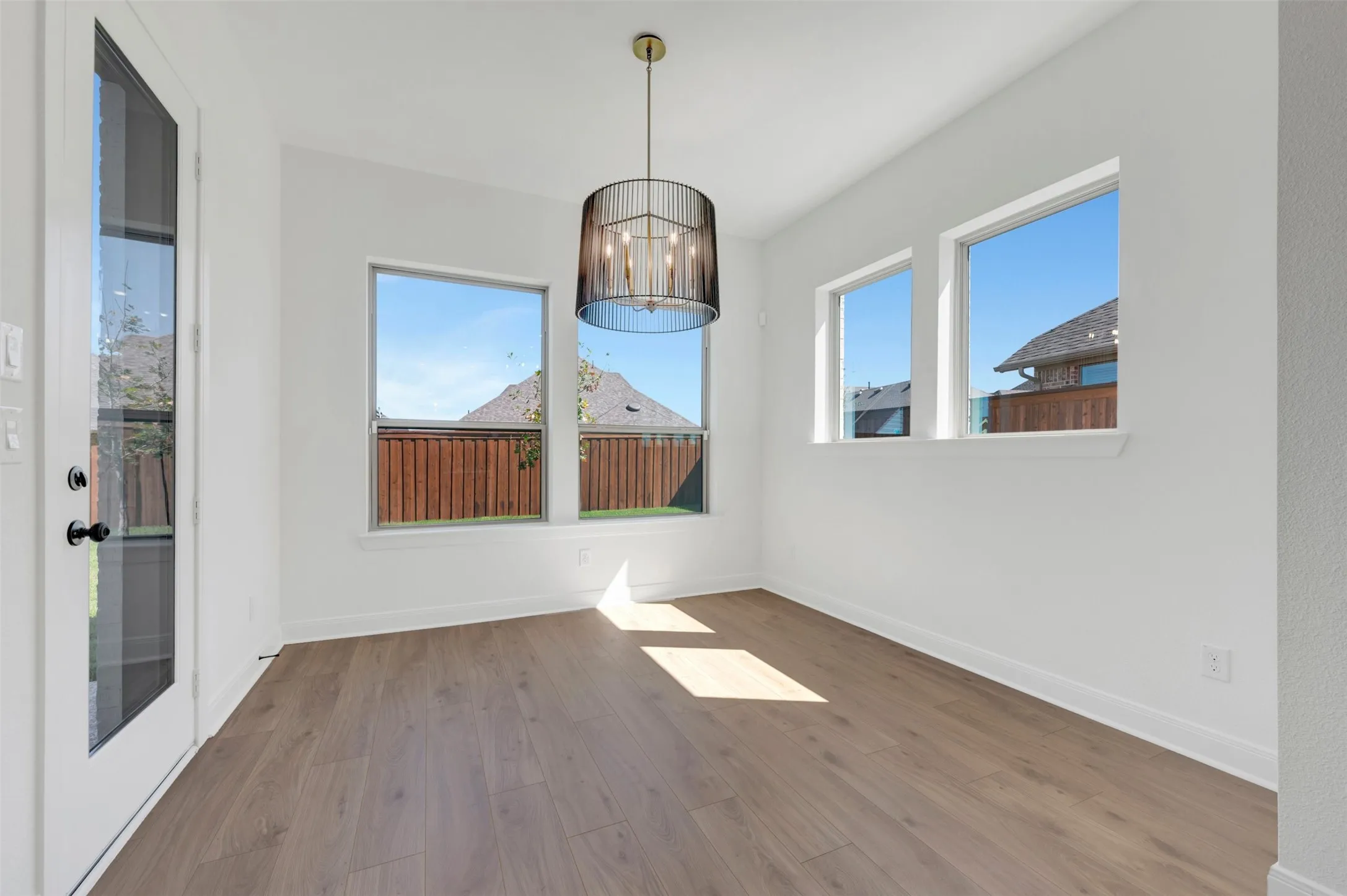 Wood-finish flooring, multiple windows, contemporary pendant light fixture, white walls, and a glass-paneled exterior door