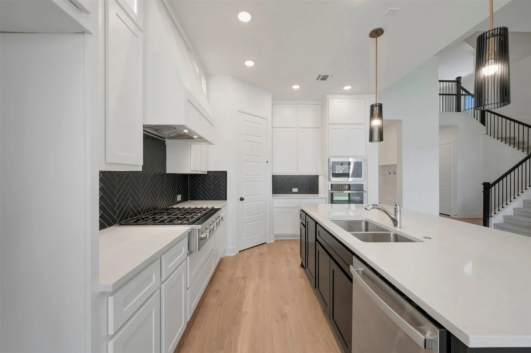 Gourmet kitchen with stainless steel appliances, herringbone tile backsplash, expansive center island, and wood-finish flooring