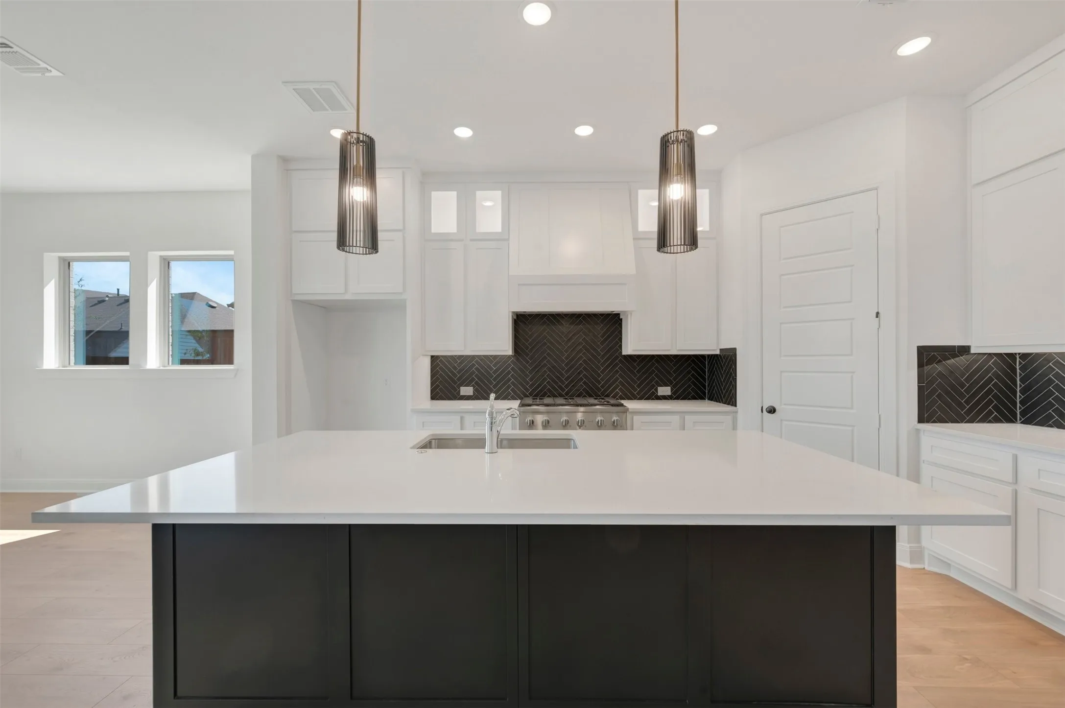 Kitchen featuring a dark-toned island, light-toned countertops, white cabinetry, a dark herringbone tile backsplash, and two hanging pendant light fixtures