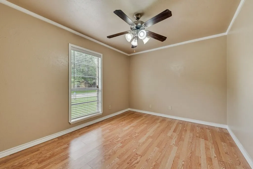 Neutral-toned room featuring a window with horizontal blinds, wood-finish flooring, a ceiling fan with integrated lighting, white baseboards, and crown molding