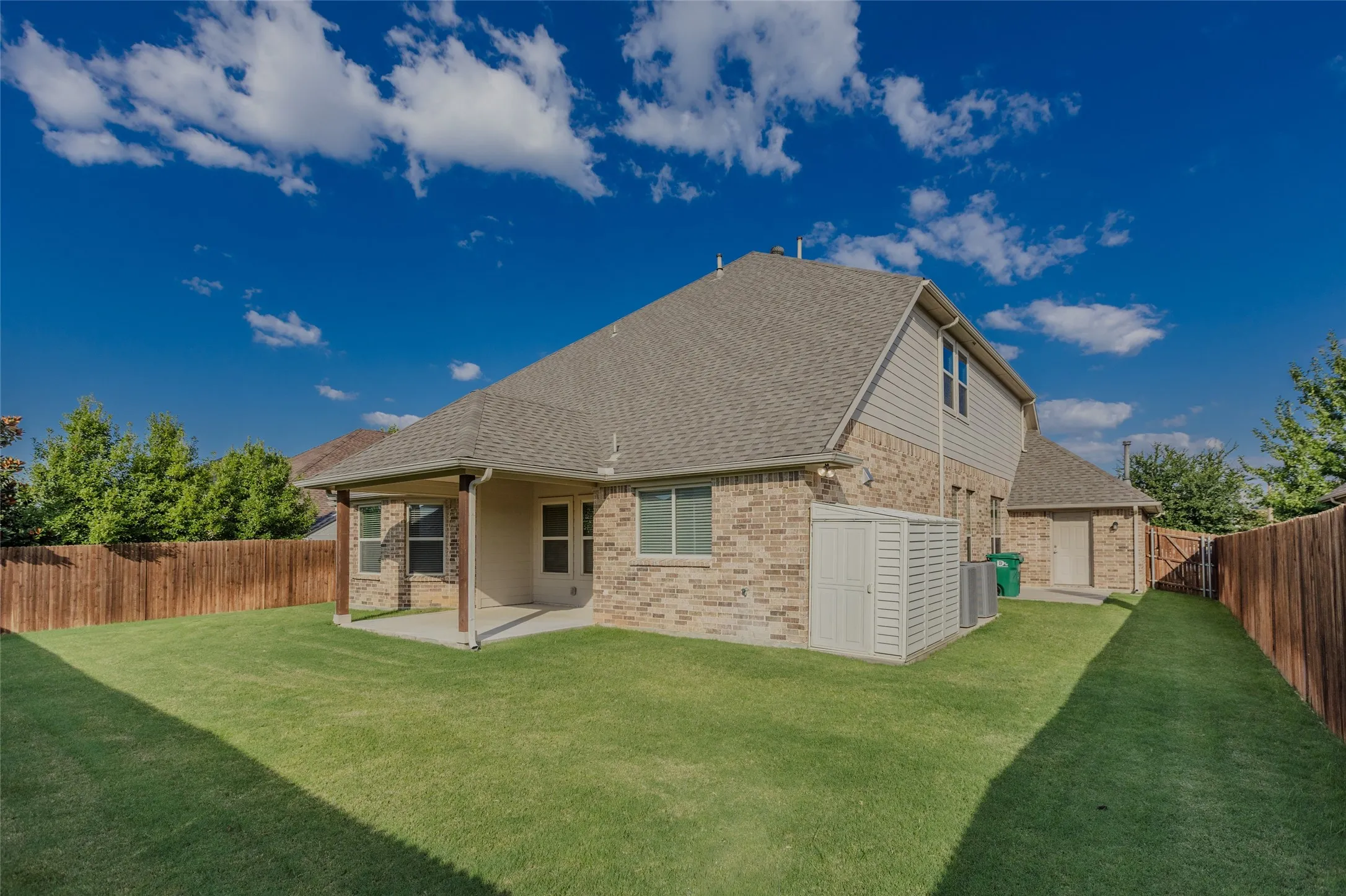 Large backyard with shed on concrete slab. Extra concrete on side near garage for garbage bins.