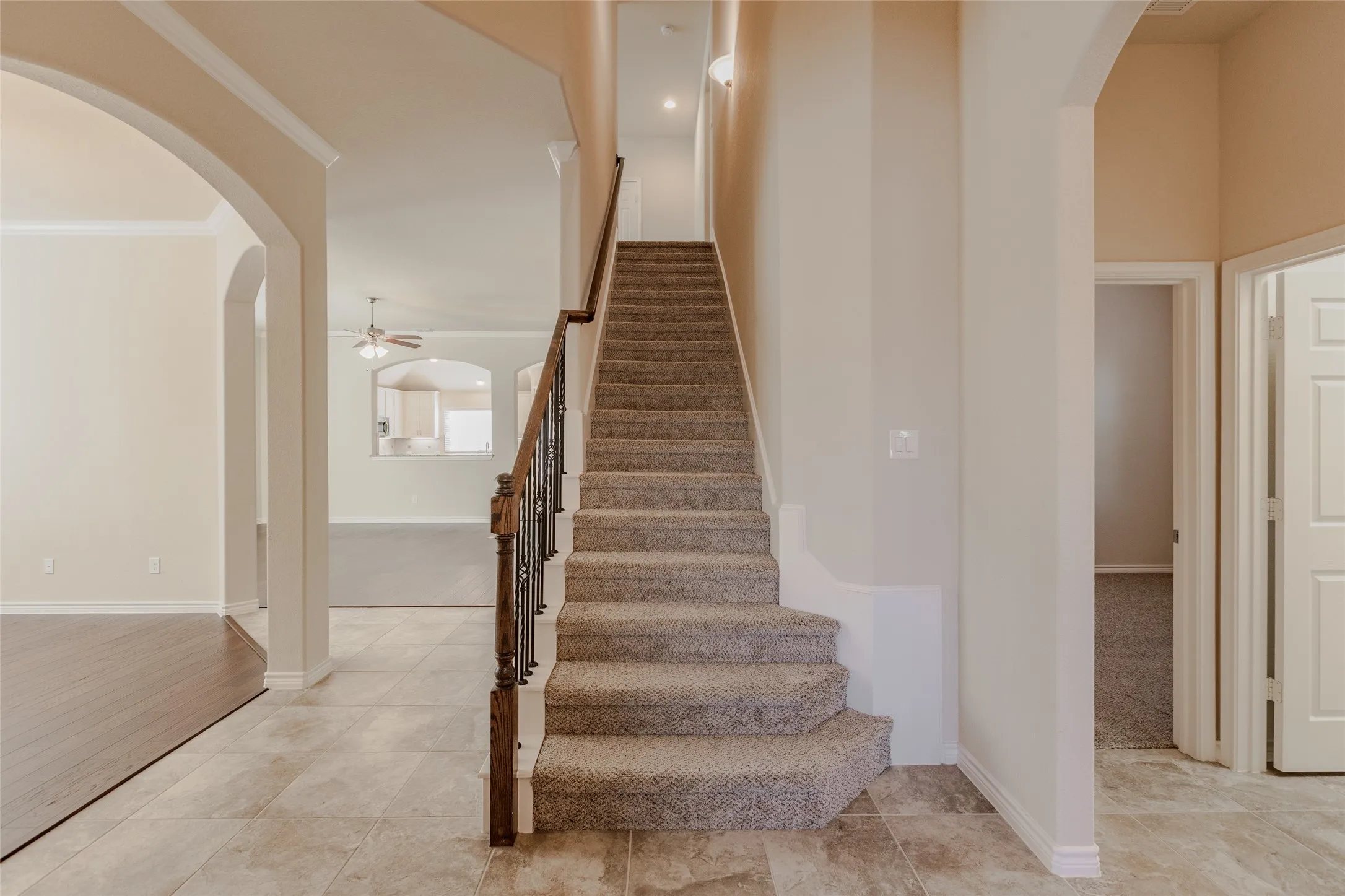 Entryway featuring a carpeted staircase with an iron and wood-finish handrail, tile flooring, and arched doorways