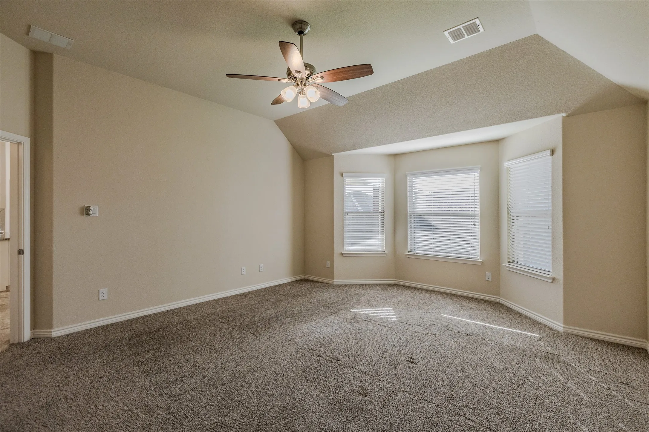 Carpeted primary bedroom on first floor featuring a ceiling fan with integrated lighting, a bay window with three individual windows, white blinds, and white baseboards