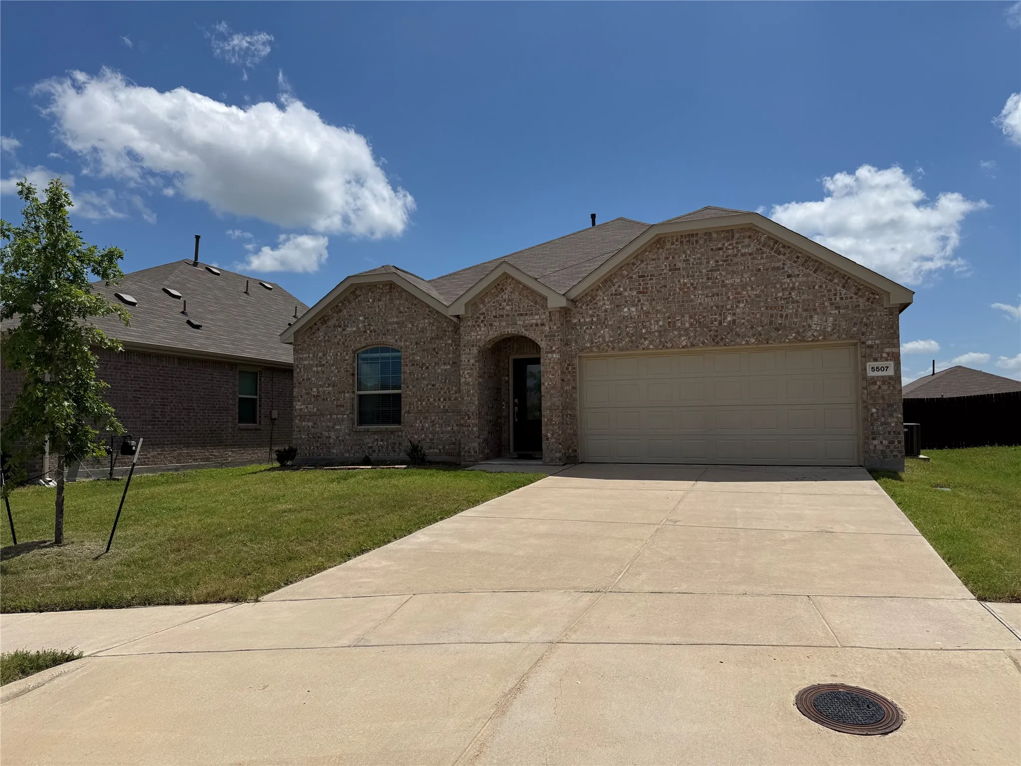 Brick facade residence featuring an arched entry, attached two-car garage, concrete driveway, and a manicured lawn
