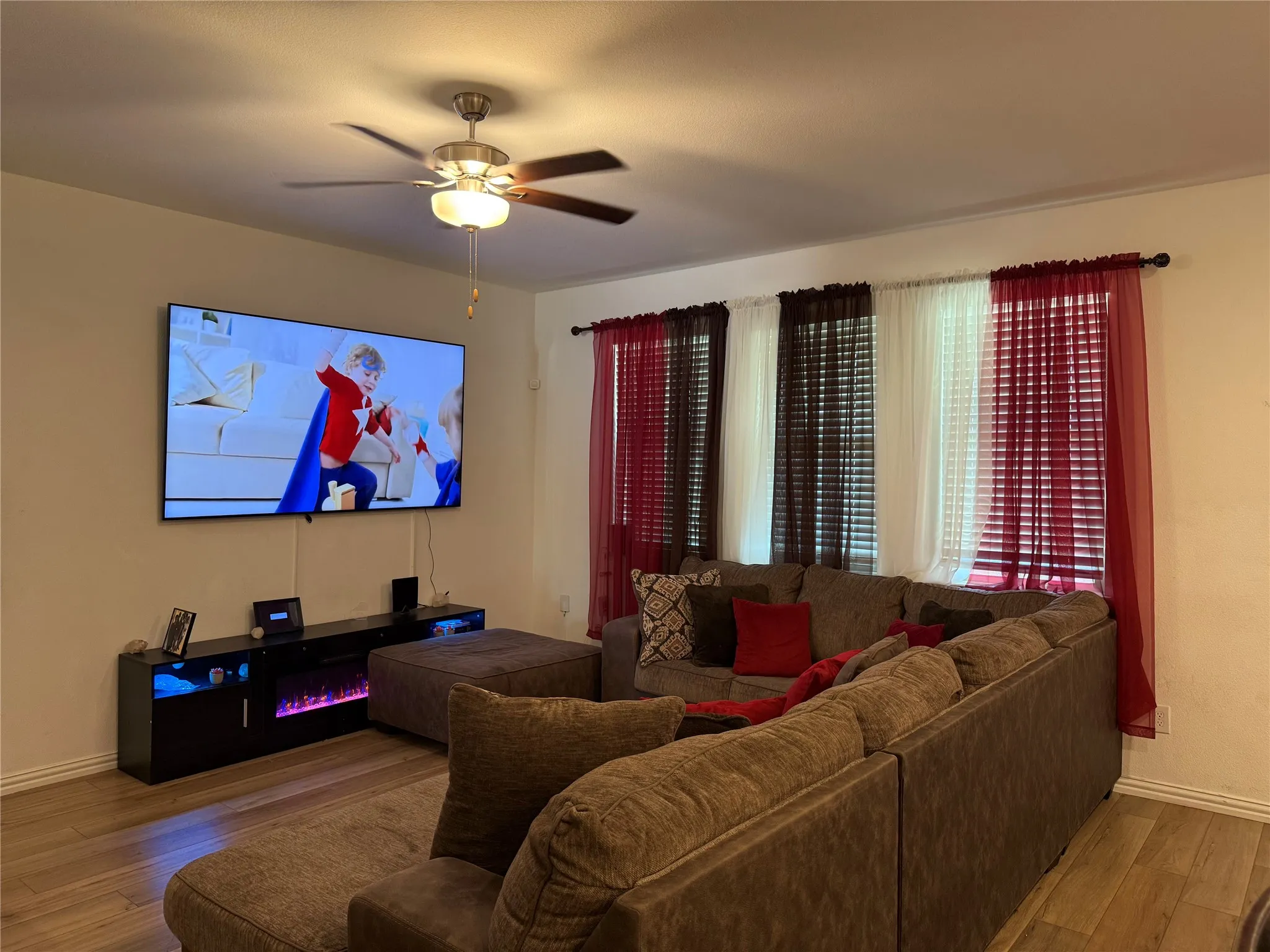 Living area featuring wood-finish flooring, a ceiling fan with integrated lighting, and multiple windows with blinds