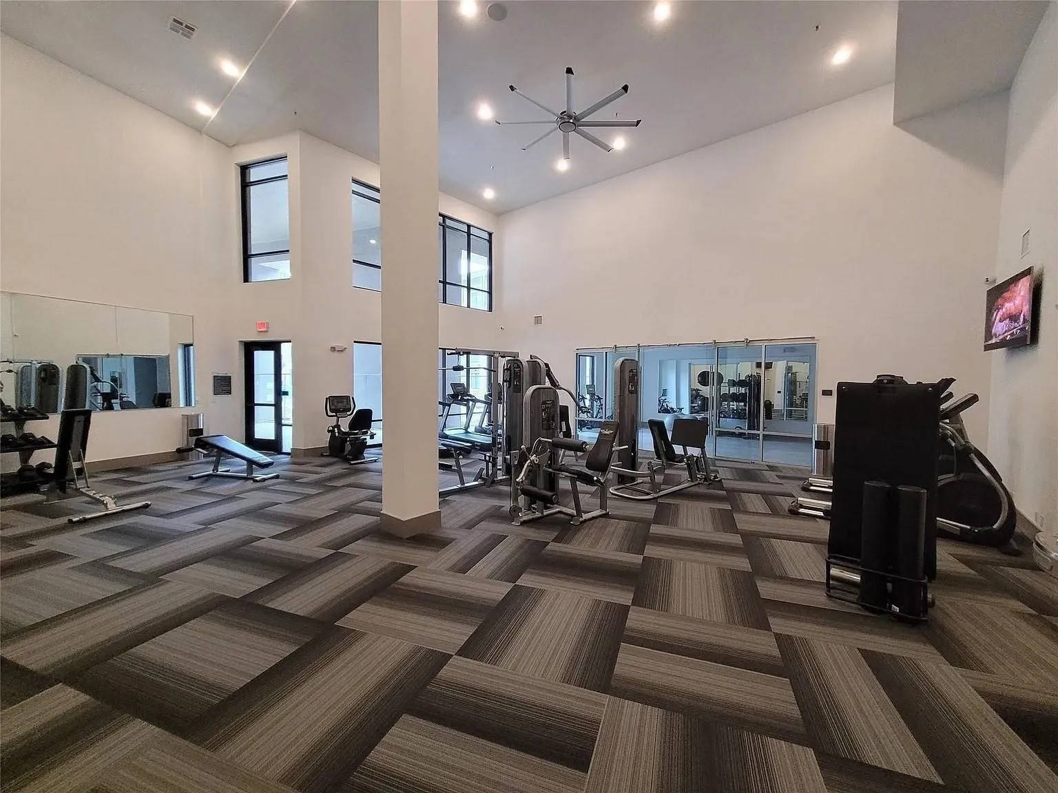 Fitness center with high ceilings, patterned carpet tile flooring, and large windows