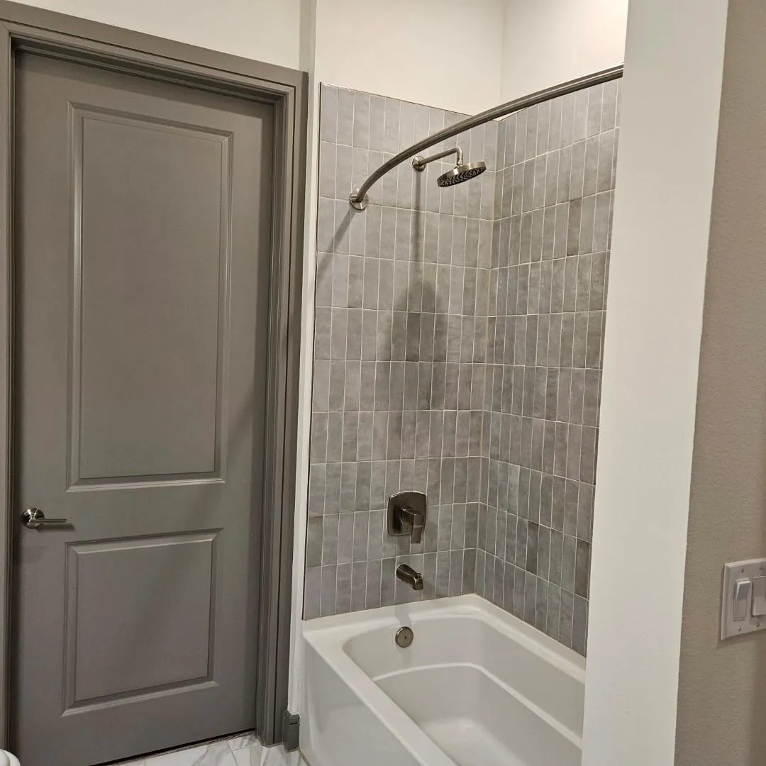 Tub/shower combination featuring vertical rectangular tile surround, brushed nickel fixtures, and a curved shower rod