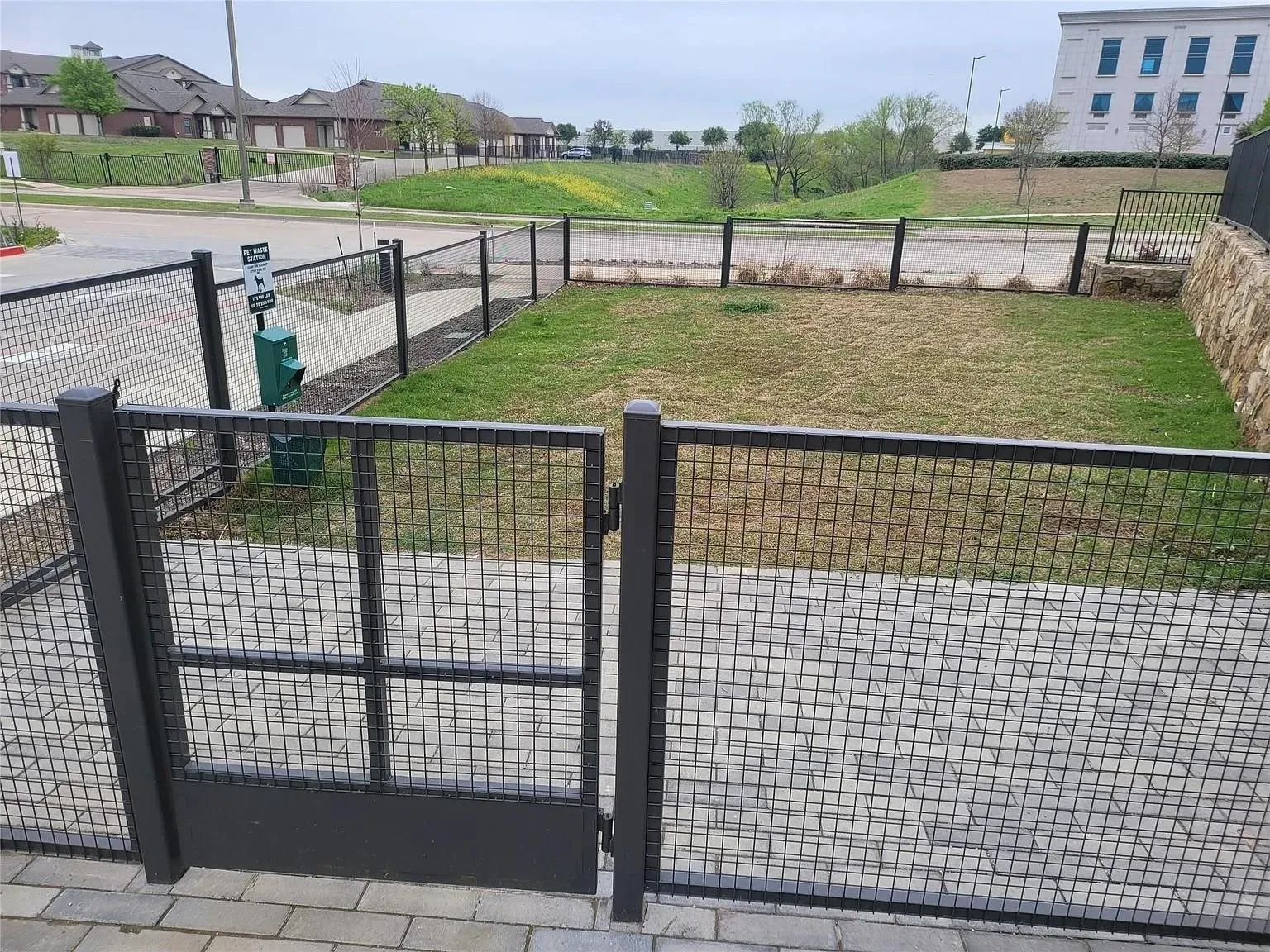 Fenced outdoor area featuring a mesh gate, paver stone walkway, and a landscaped grassy section