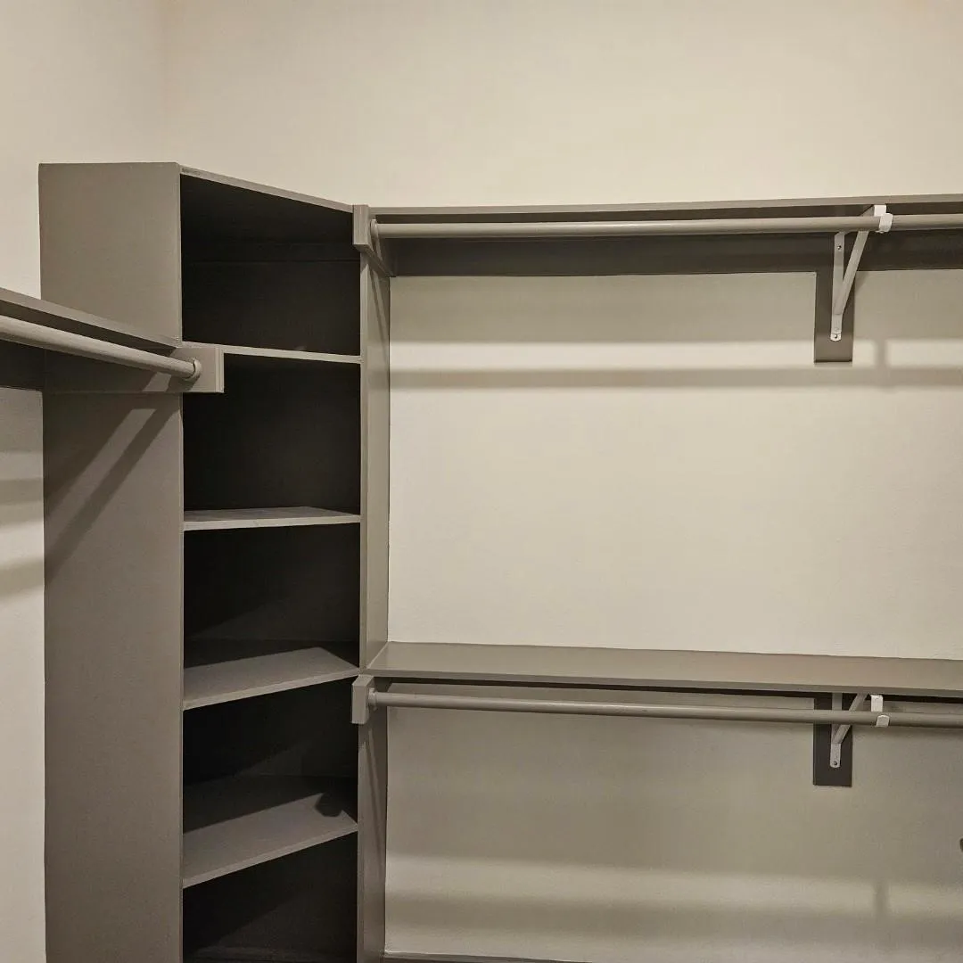 Built-in closet system featuring multiple hanging rods, corner shelving, and neutral tone finishes