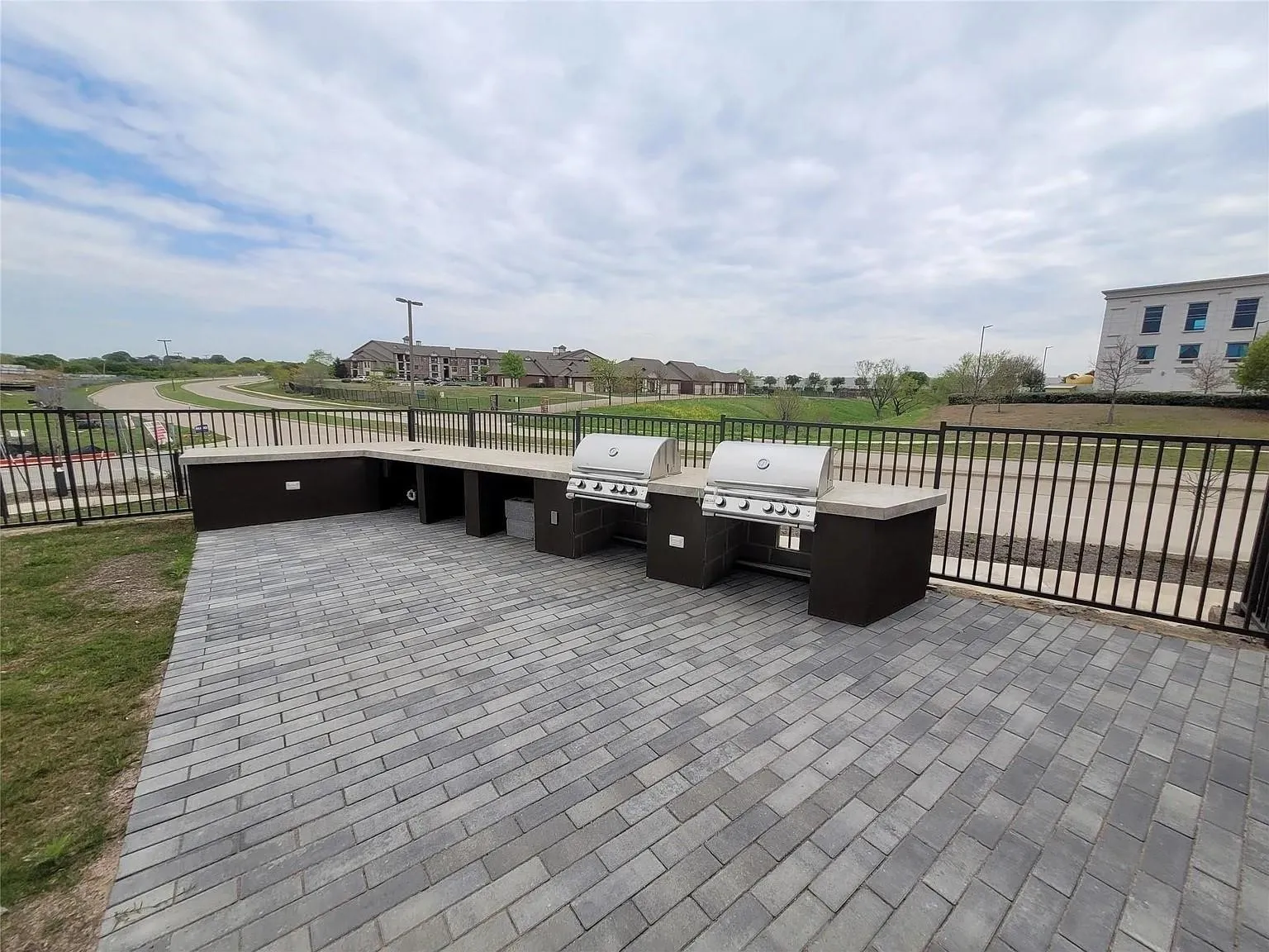 Expansive outdoor kitchen featuring two built-in grills, a large counter space, and integrated storage, all set on a durable paver patio