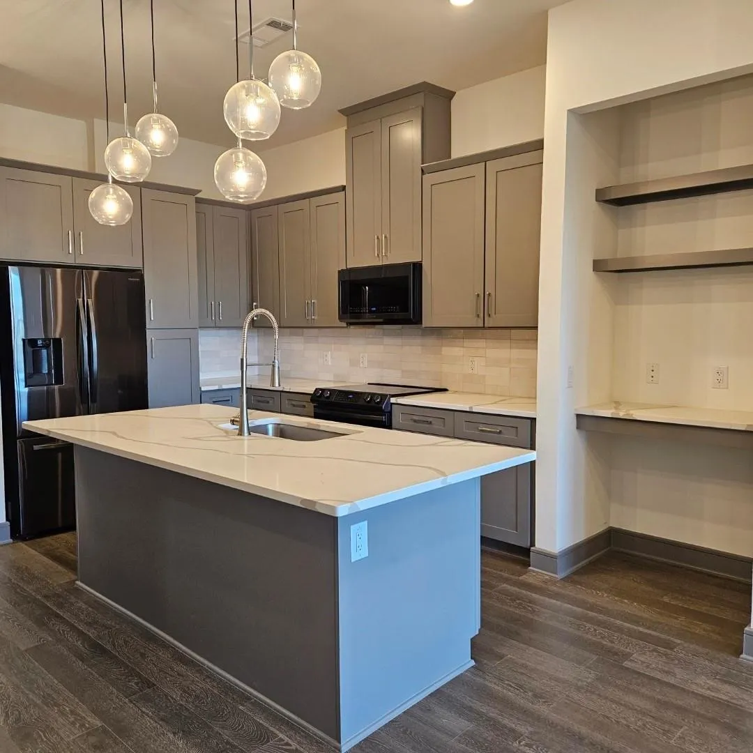 Kitchen featuring a center island with sink, white countertops, gray cabinetry, and a full suite of black kitchen appliances
