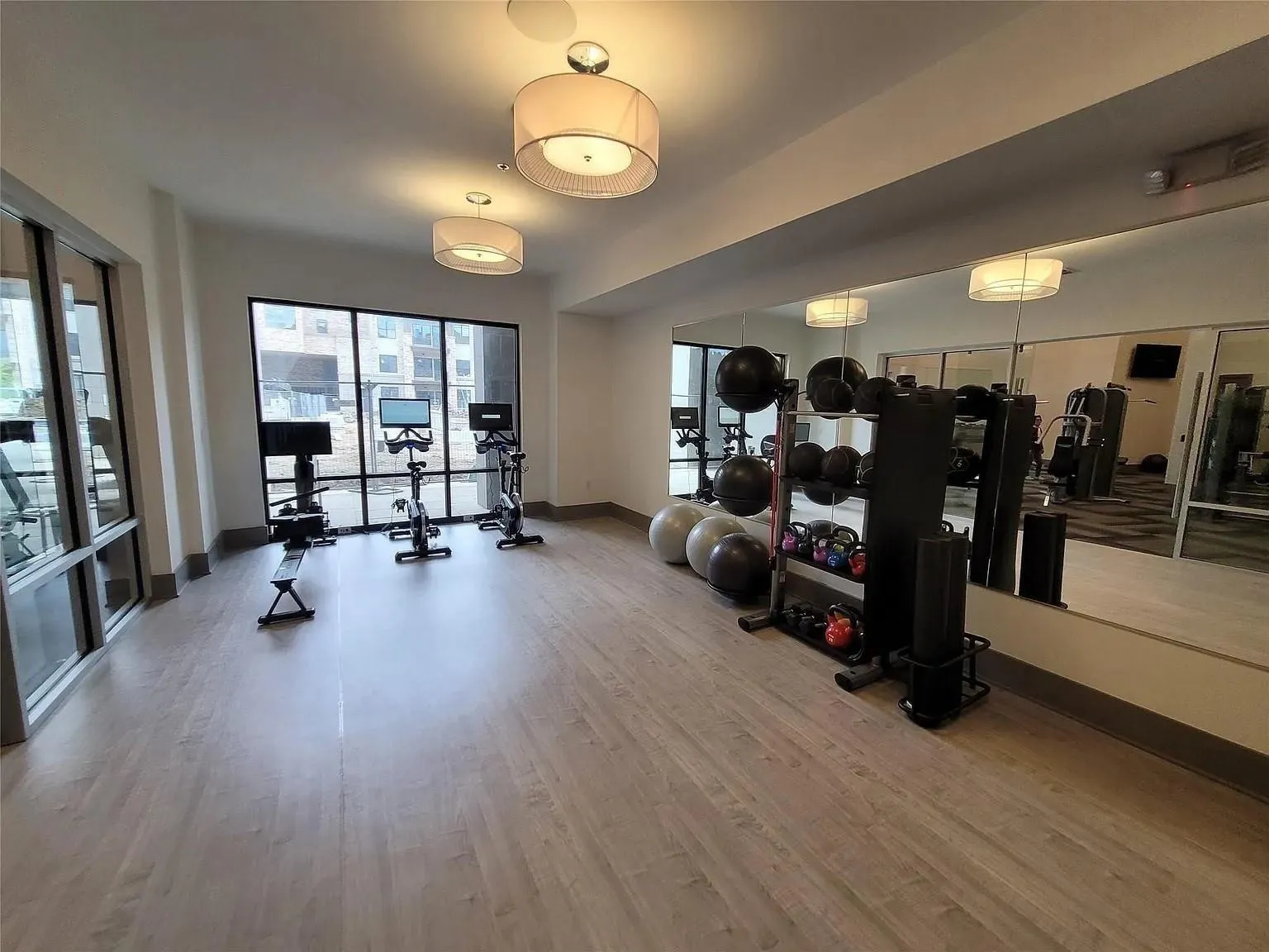 Dedicated fitness space featuring wood-finish flooring, full-height mirrored wall, and large windows providing natural light