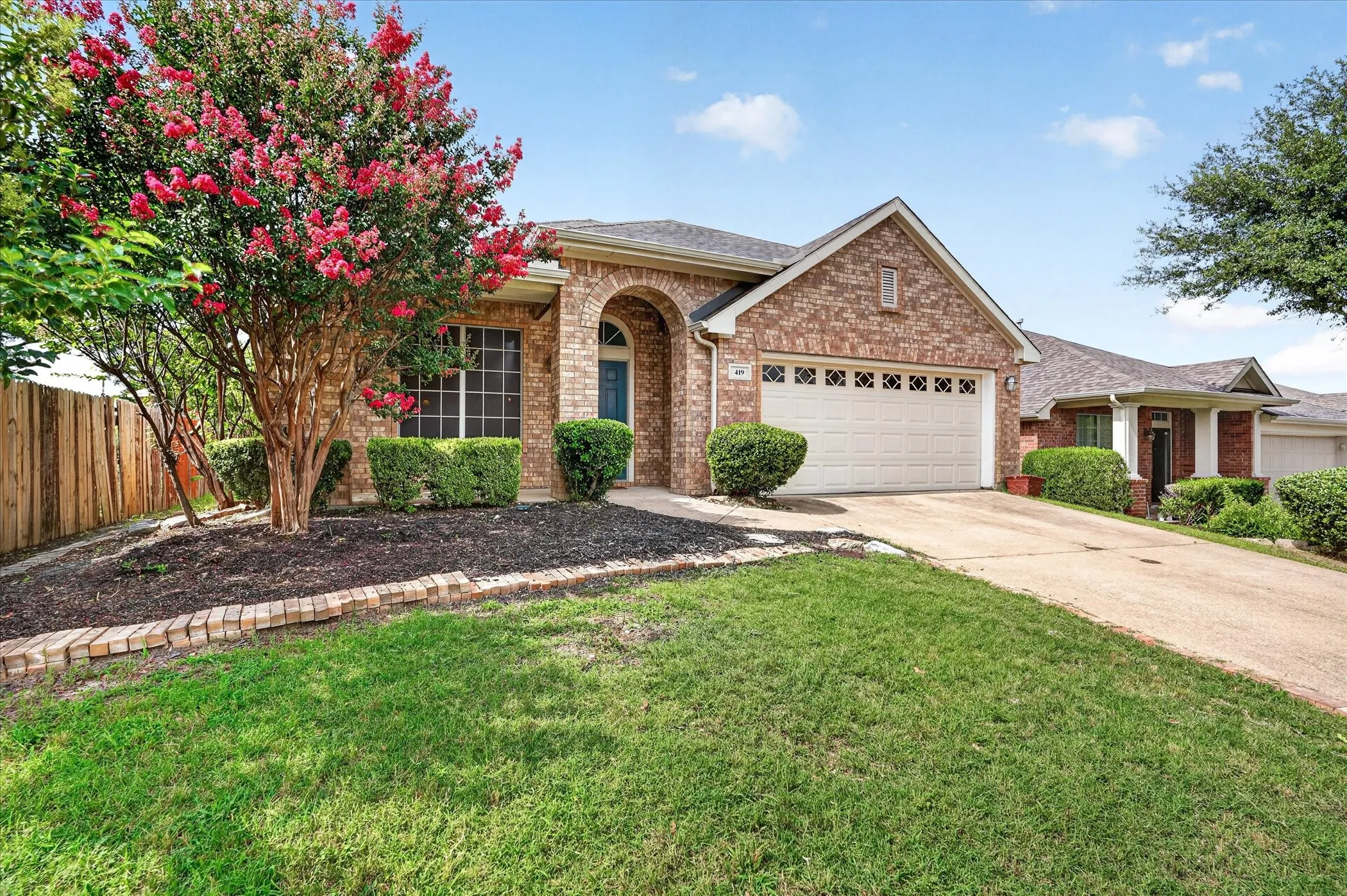 Brick exterior home featuring a two-car garage, an arched entryway, and a mature flowering tree