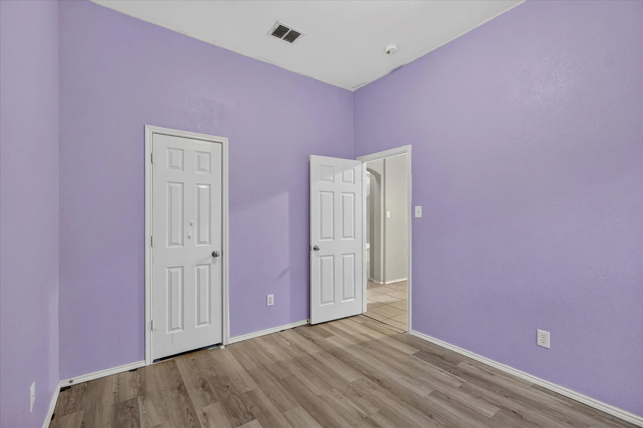 Room featuring wood-finish flooring, two paneled doors, and a ceiling-mounted air vent