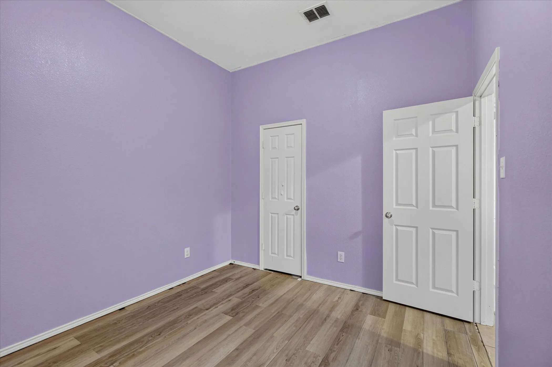 Room featuring light wood-finish flooring, purple painted walls, and white trim