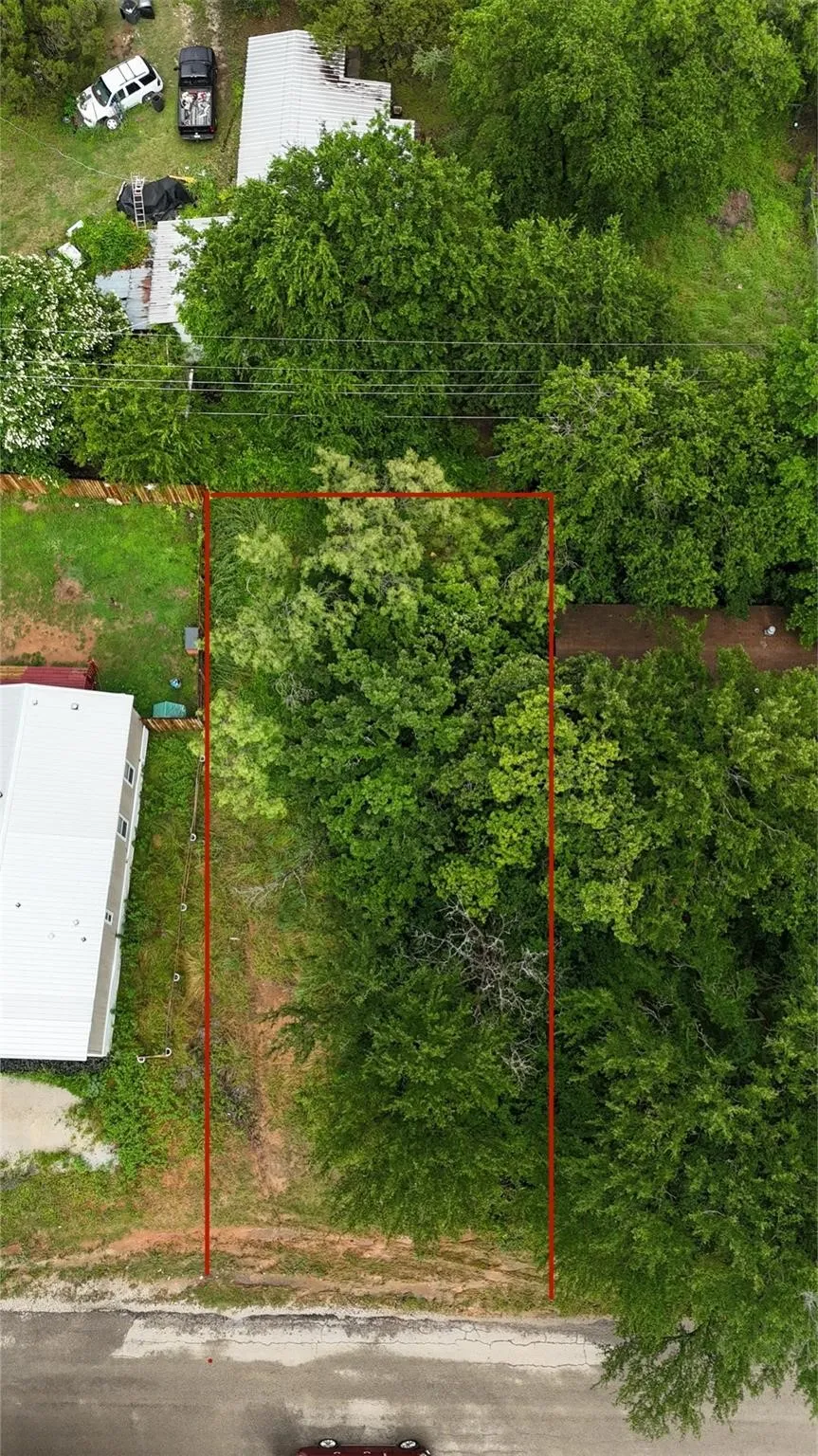 Vacant land parcel featuring mature trees and a partial grass cover