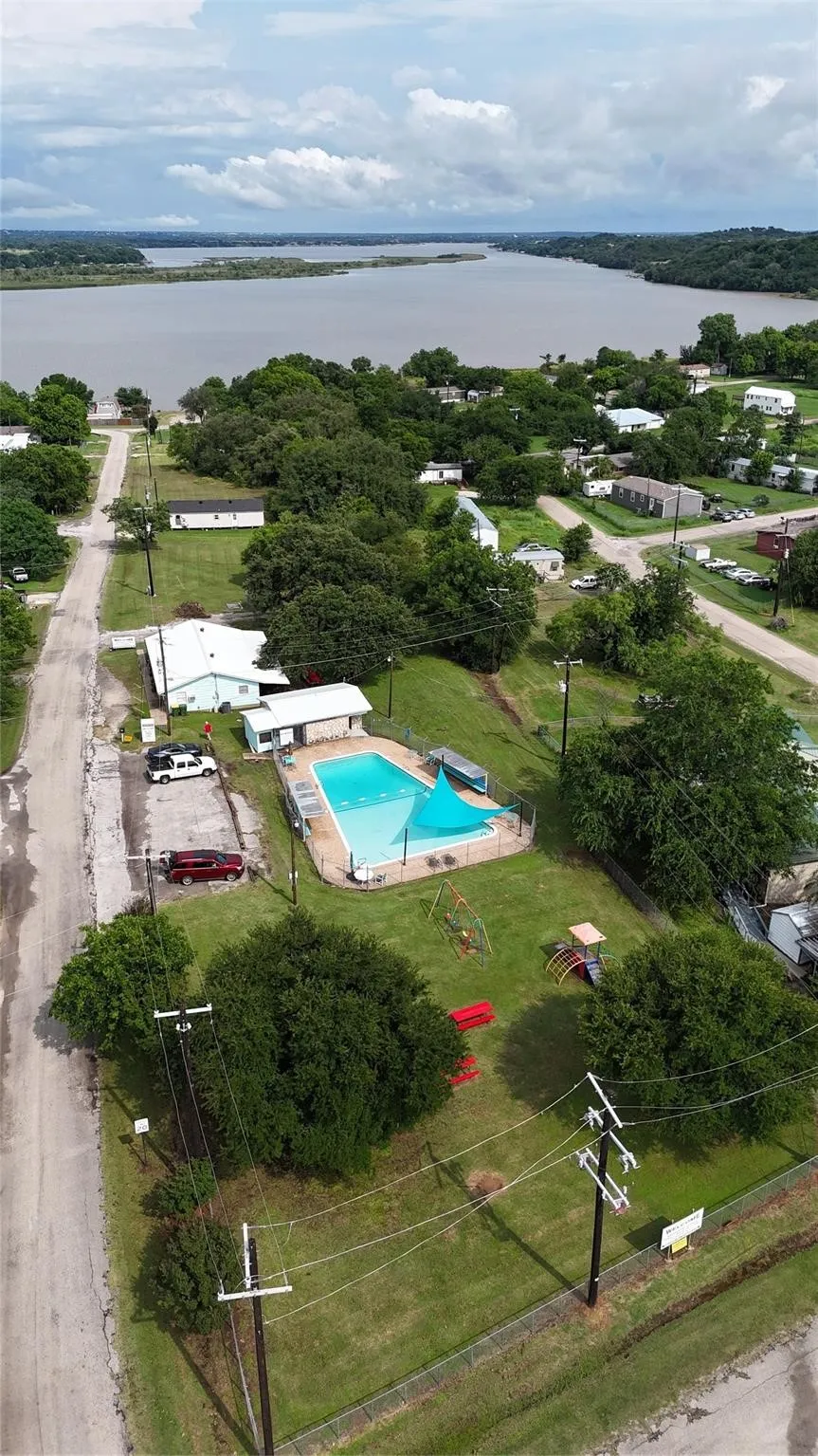 Expansive community grounds featuring a large rectangular swimming pool with safety fencing, a shaded children's play area, and a grassy lawn with mature trees