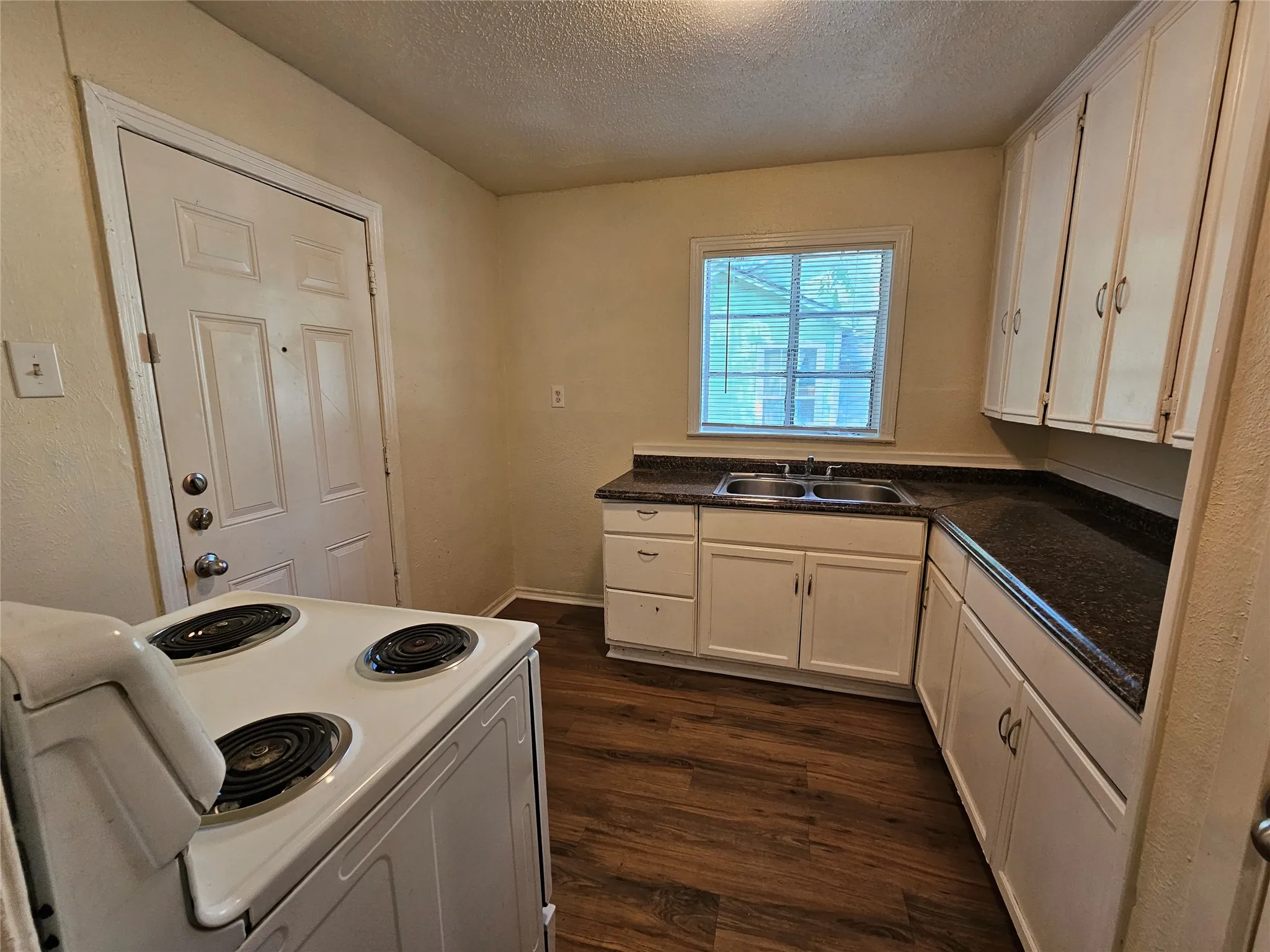 Kitchen featuring white cabinetry, dark countertops, wood-finish flooring, and a double basin sink beneath a window