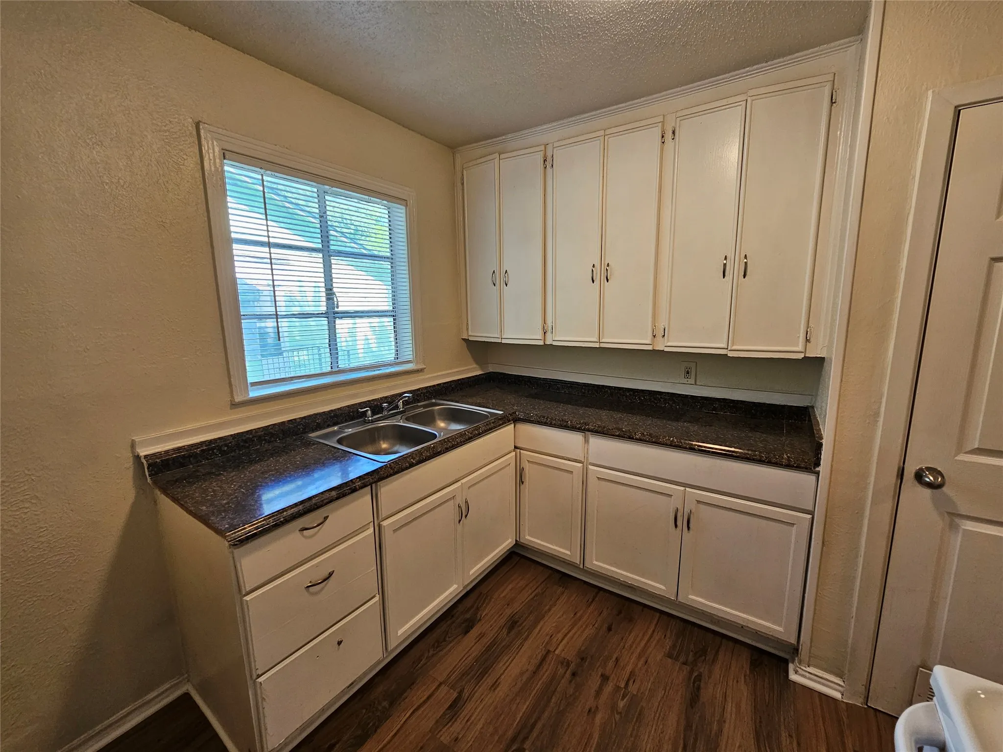 Kitchen featuring extensive white cabinetry, dark speckled countertops, and wood-finish flooring