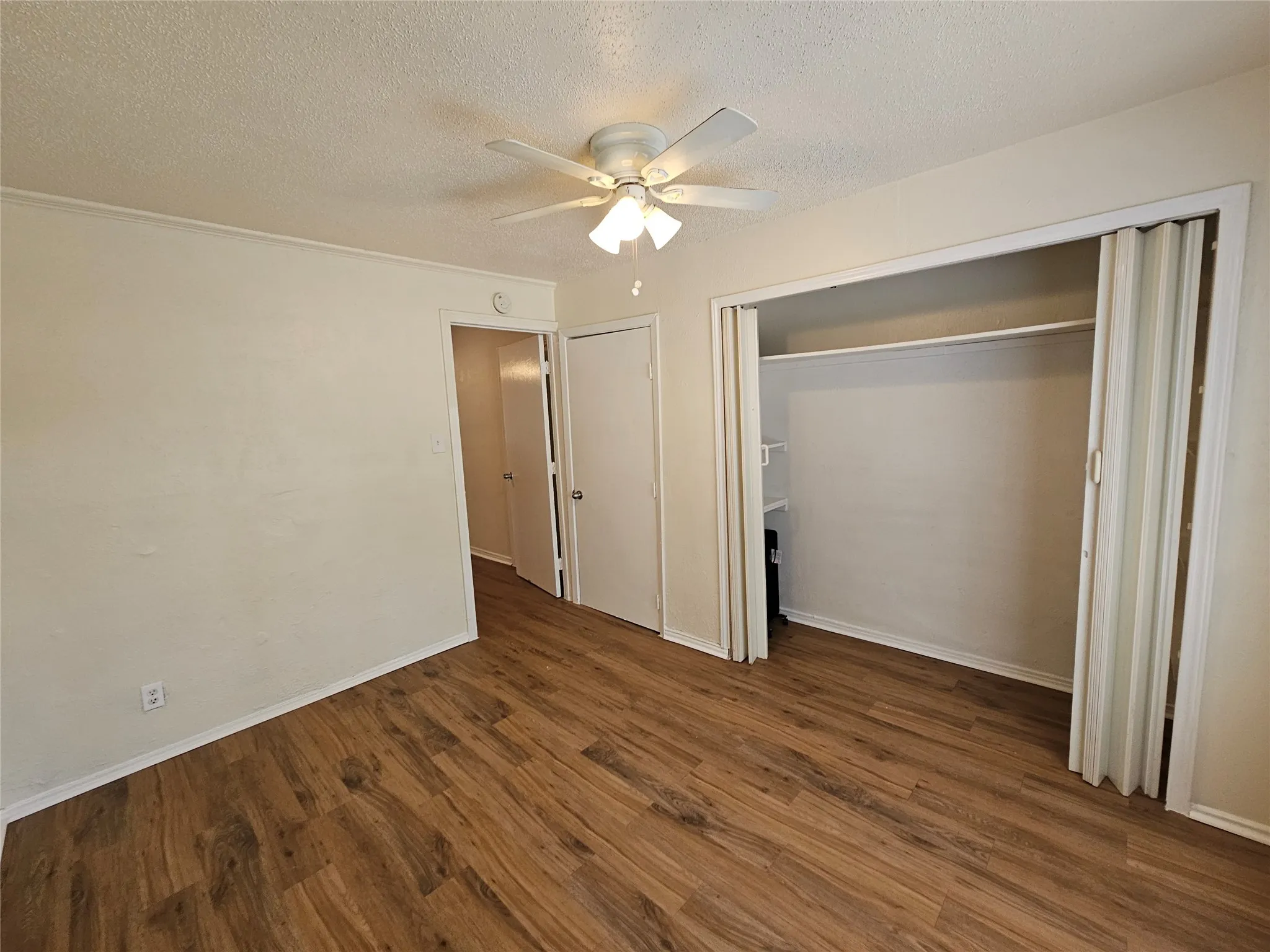 Spacious room featuring wood-finish flooring, a ceiling fan with integrated lighting, and a bi-fold closet