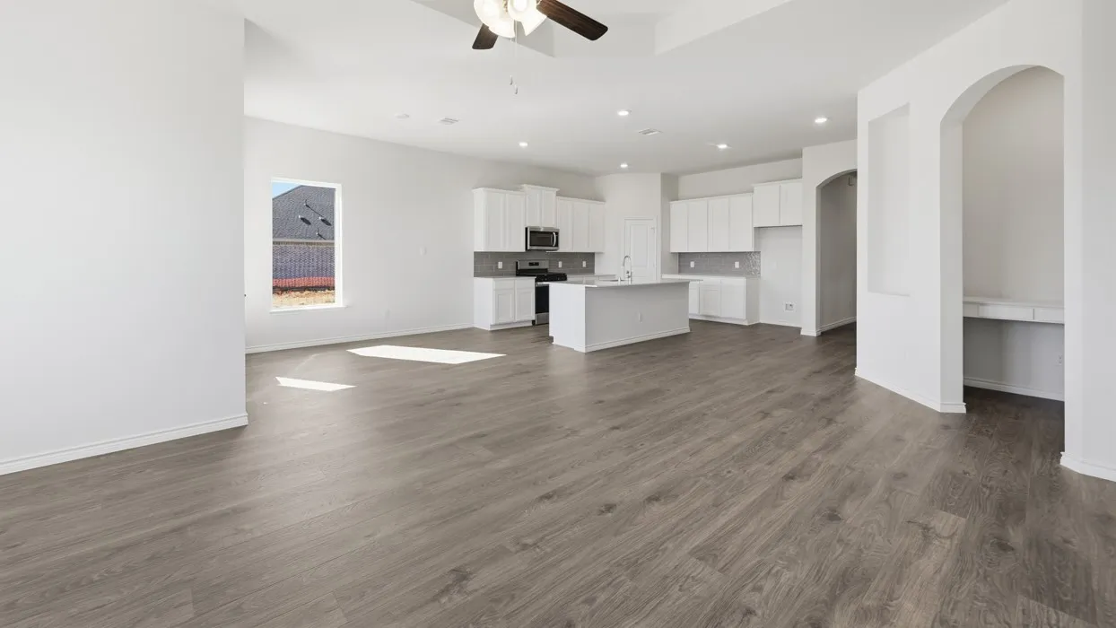 Open-concept living space featuring wood-finish flooring, a contemporary kitchen with white cabinetry and a central island, recessed lighting, and a built-in archway desk area