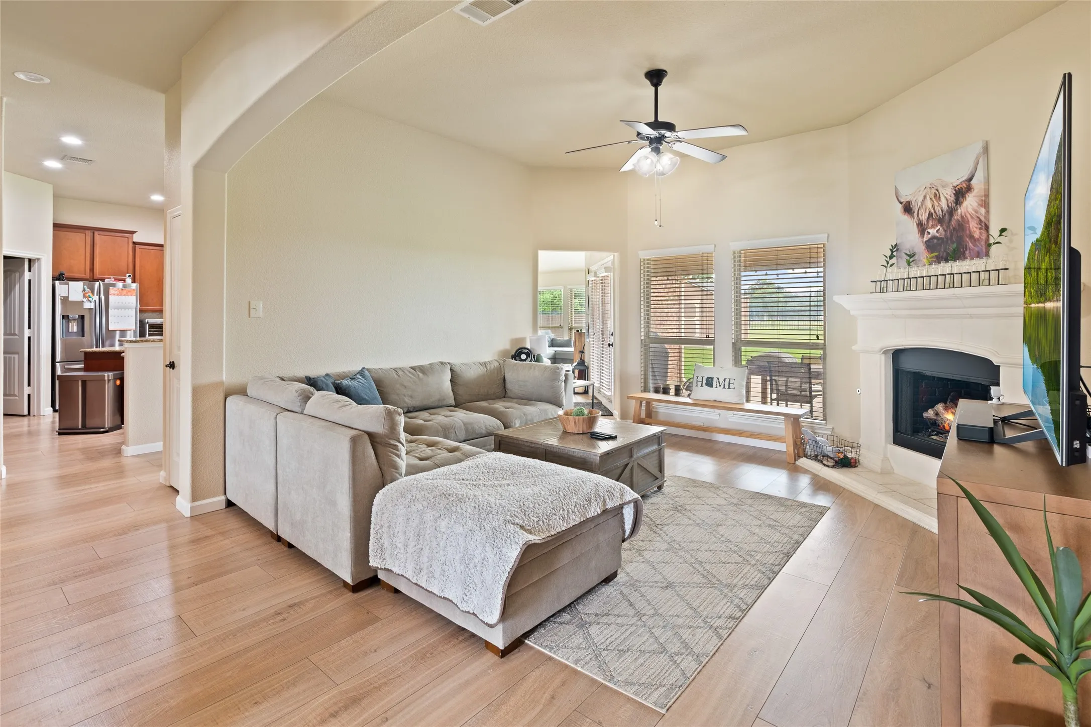 Living area featuring wood-finish flooring, a ceiling fan with integrated lighting, and a fireplace with a detailed mantel