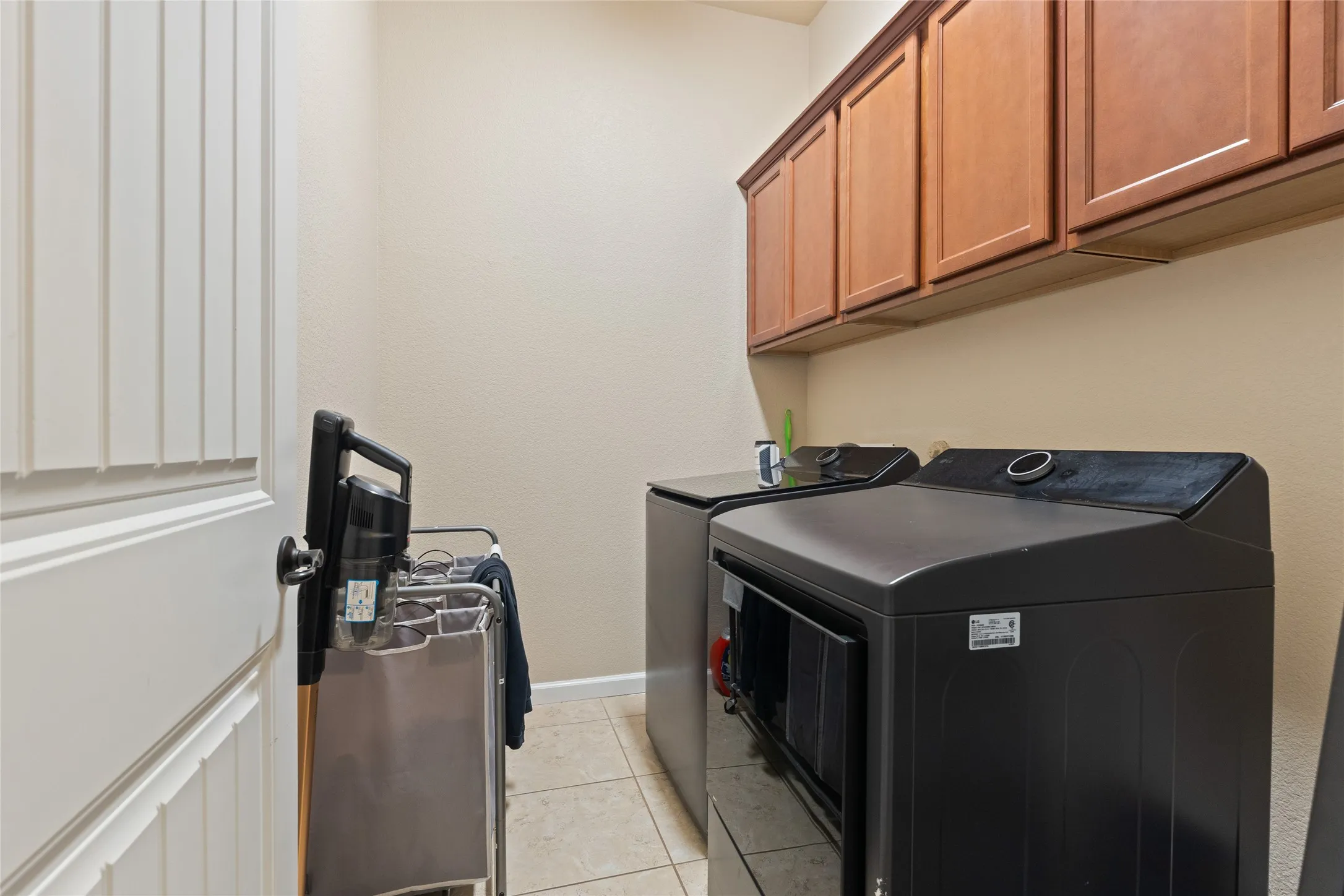 Laundry area featuring overhead wood-finish cabinetry, neutral wall color, and tile flooring