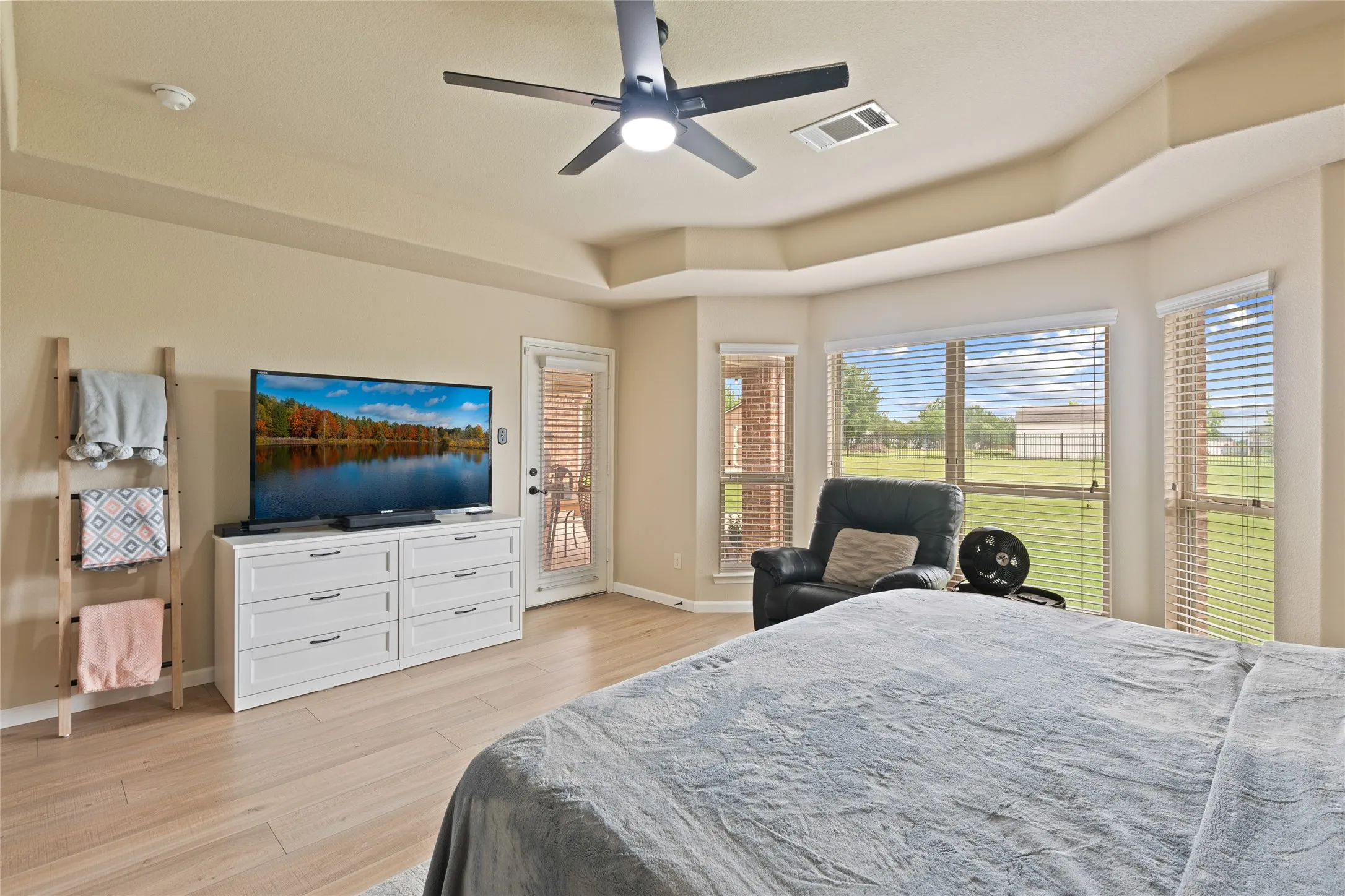 Spacious room featuring wood-finish flooring, a tray ceiling, and a ceiling fan with integrated lighting