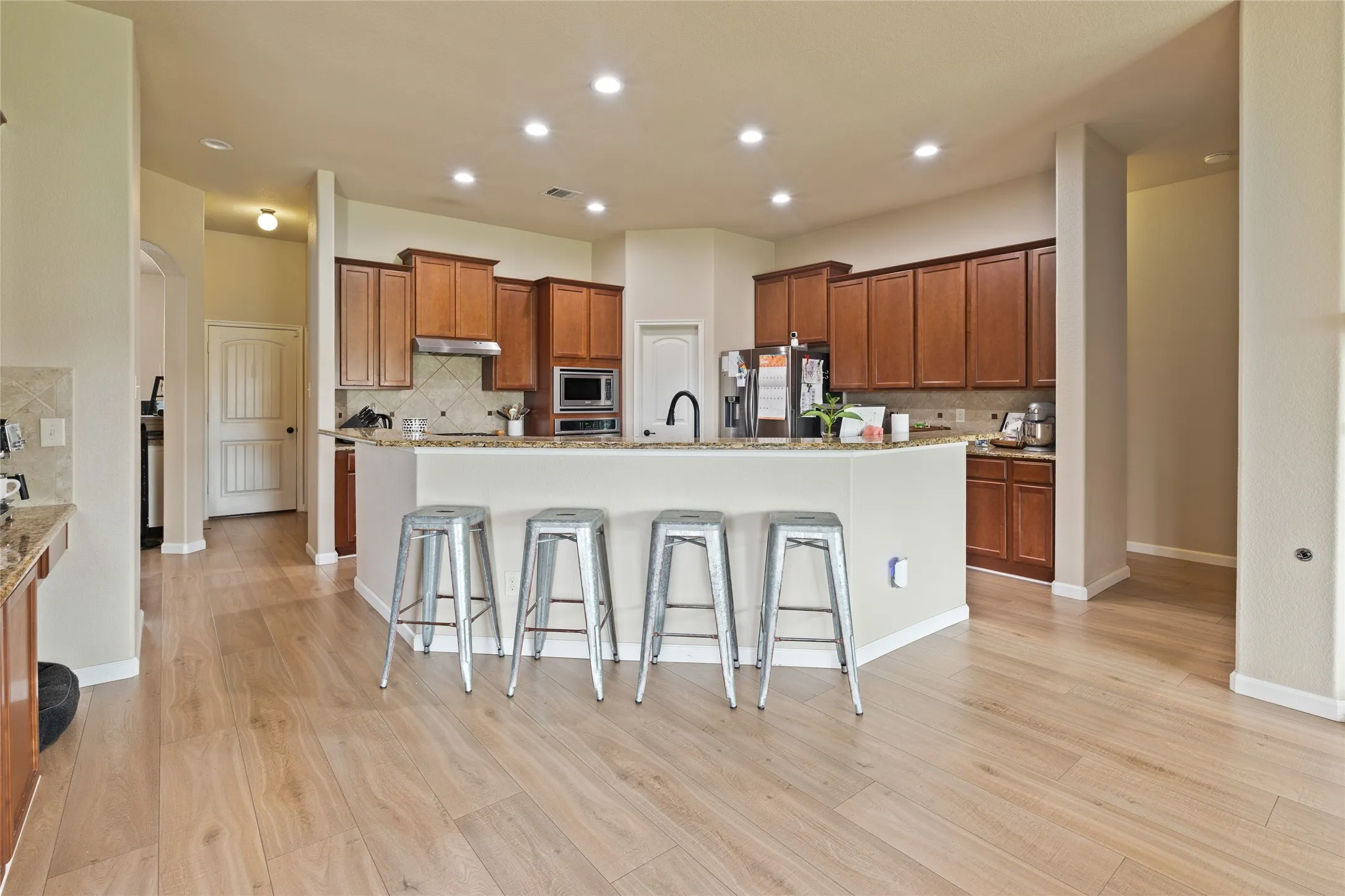 Open-concept kitchen featuring wood-finish flooring, recessed lighting, and a breakfast bar with stone countertops