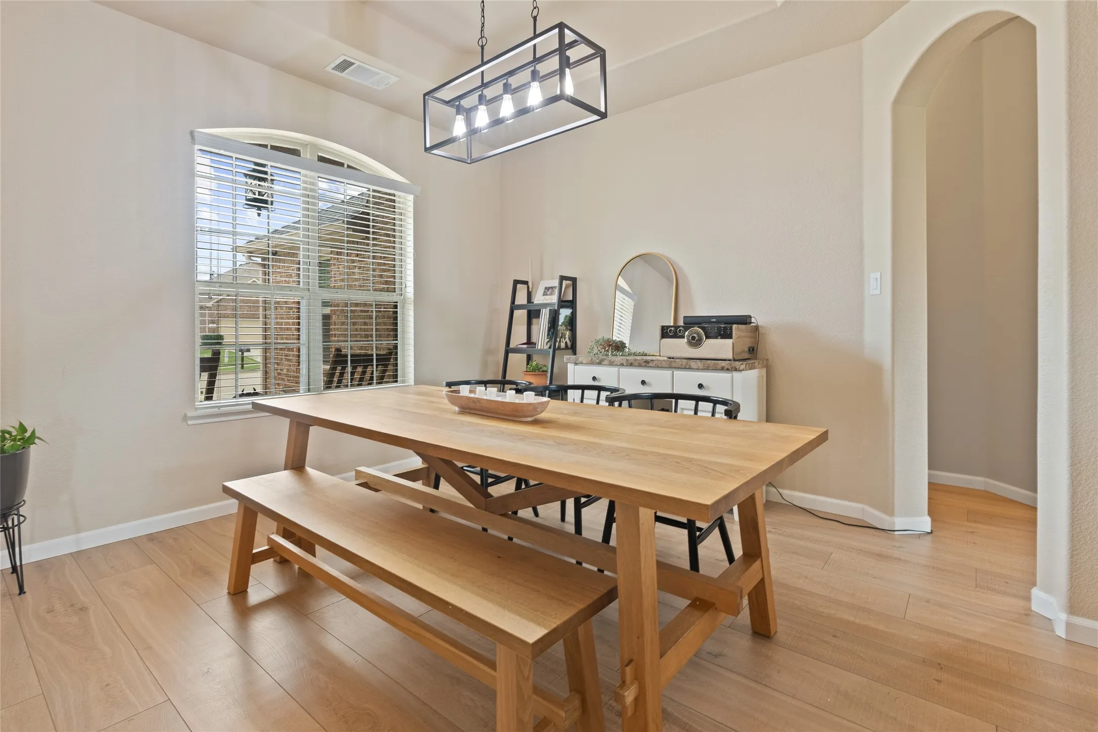 Spacious interior featuring wood-finish flooring, a contemporary linear chandelier, an arched doorway, and an arched window with blinds