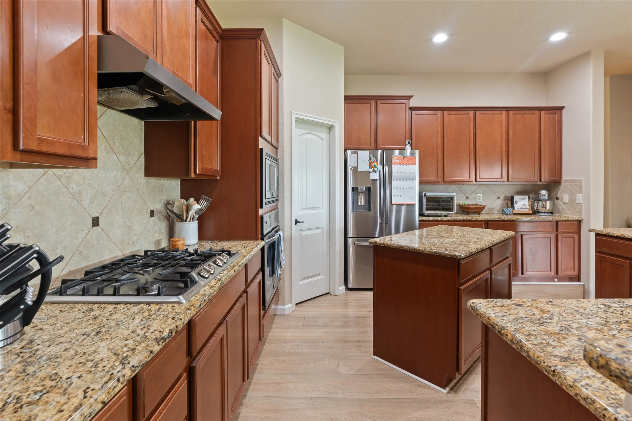 Kitchen featuring granite countertops, wood-finish flooring, stainless steel appliances, a built-in gas cooktop, and abundant cabinetry