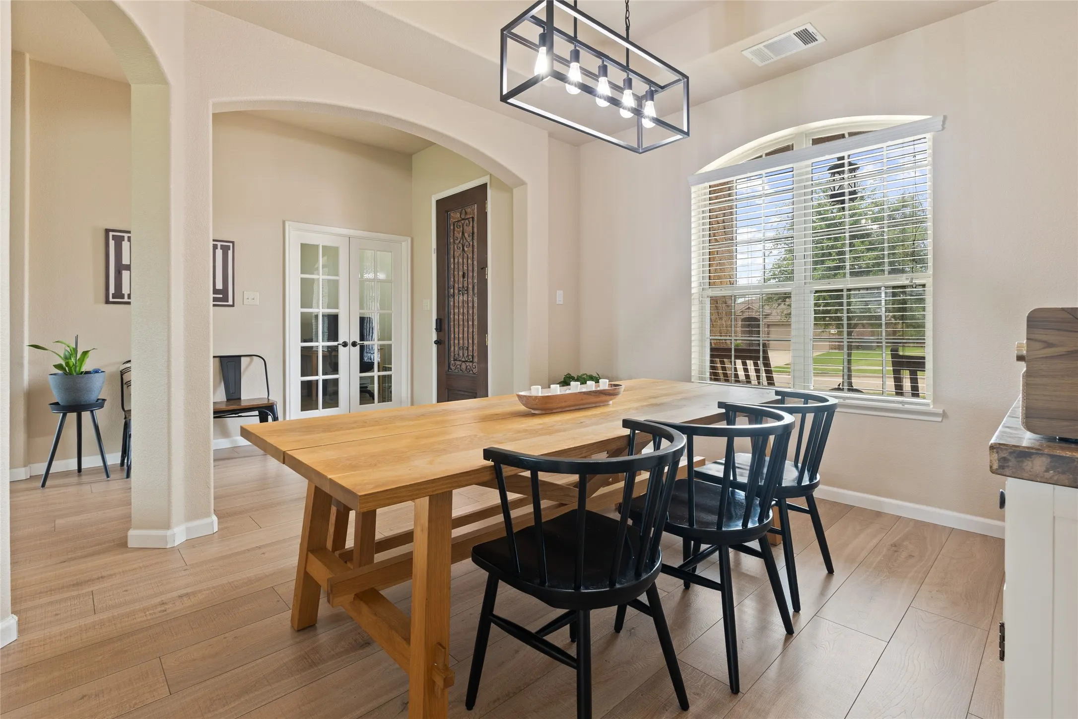 Dining area featuring wood-finish flooring, a contemporary linear chandelier, an arched window with blinds, and neutral wall tones