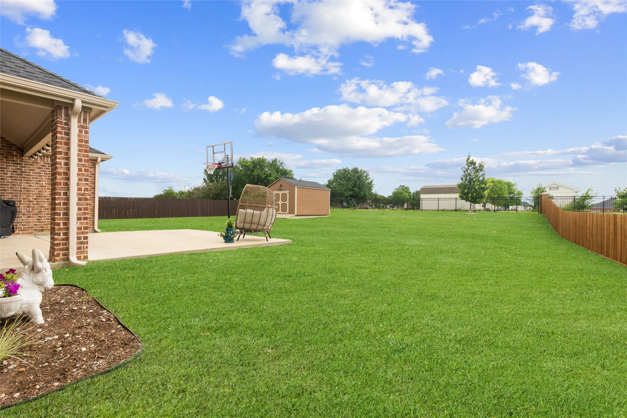 Expansive green space featuring a concrete patio, brick exterior, and a wood-panel fence