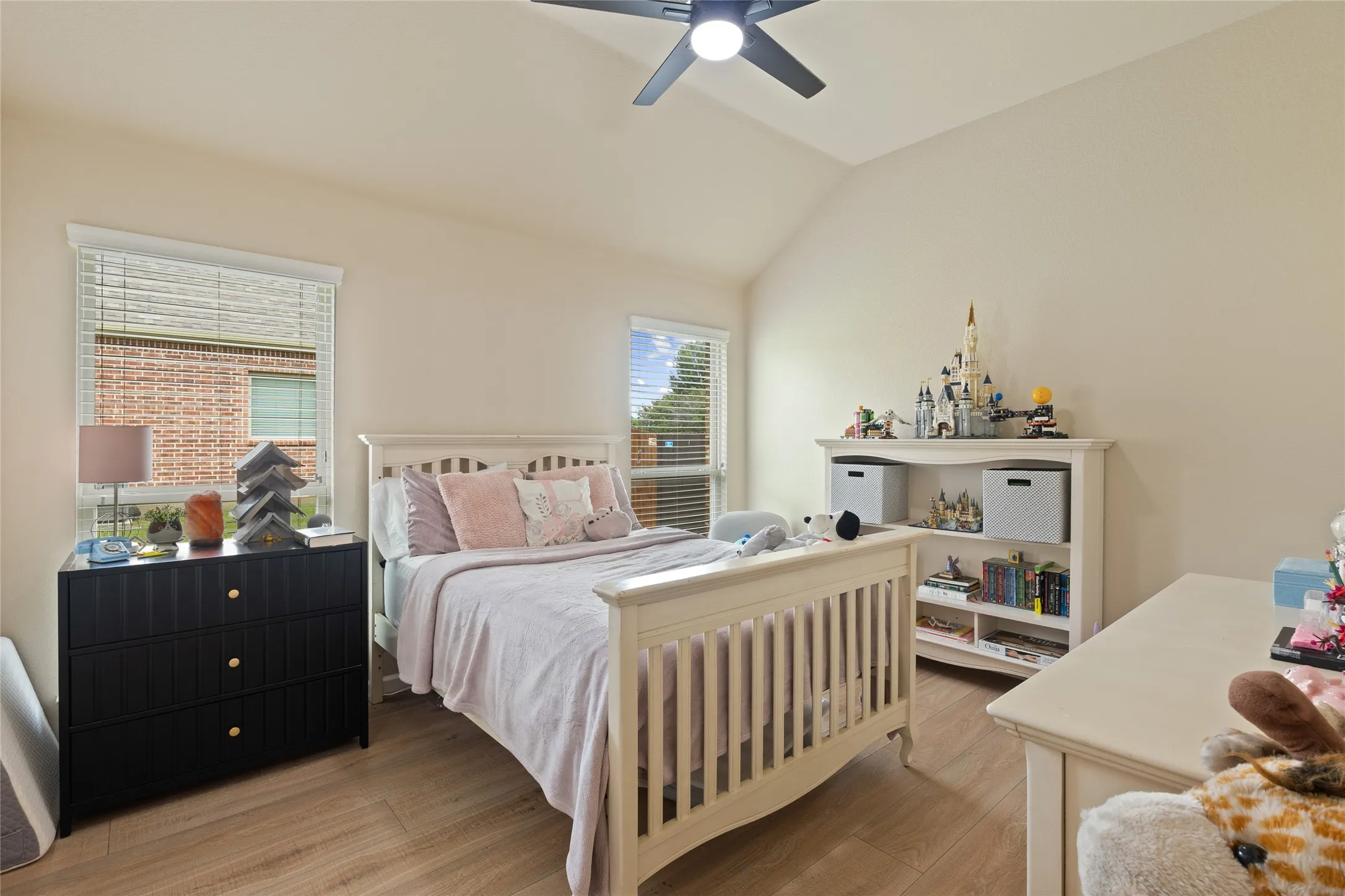 Vaulted ceiling bedroom with wood-finish flooring, two windows with blinds, and a ceiling fan with integrated lighting
