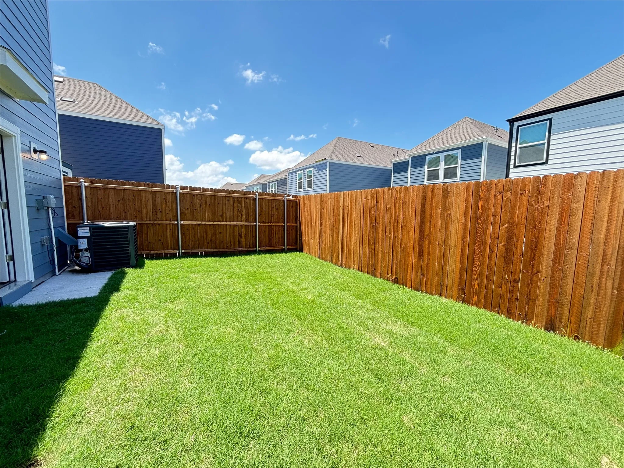 Fenced backyard featuring a manicured lawn, a concrete patio area, and a privacy fence constructed from vertical wood planks