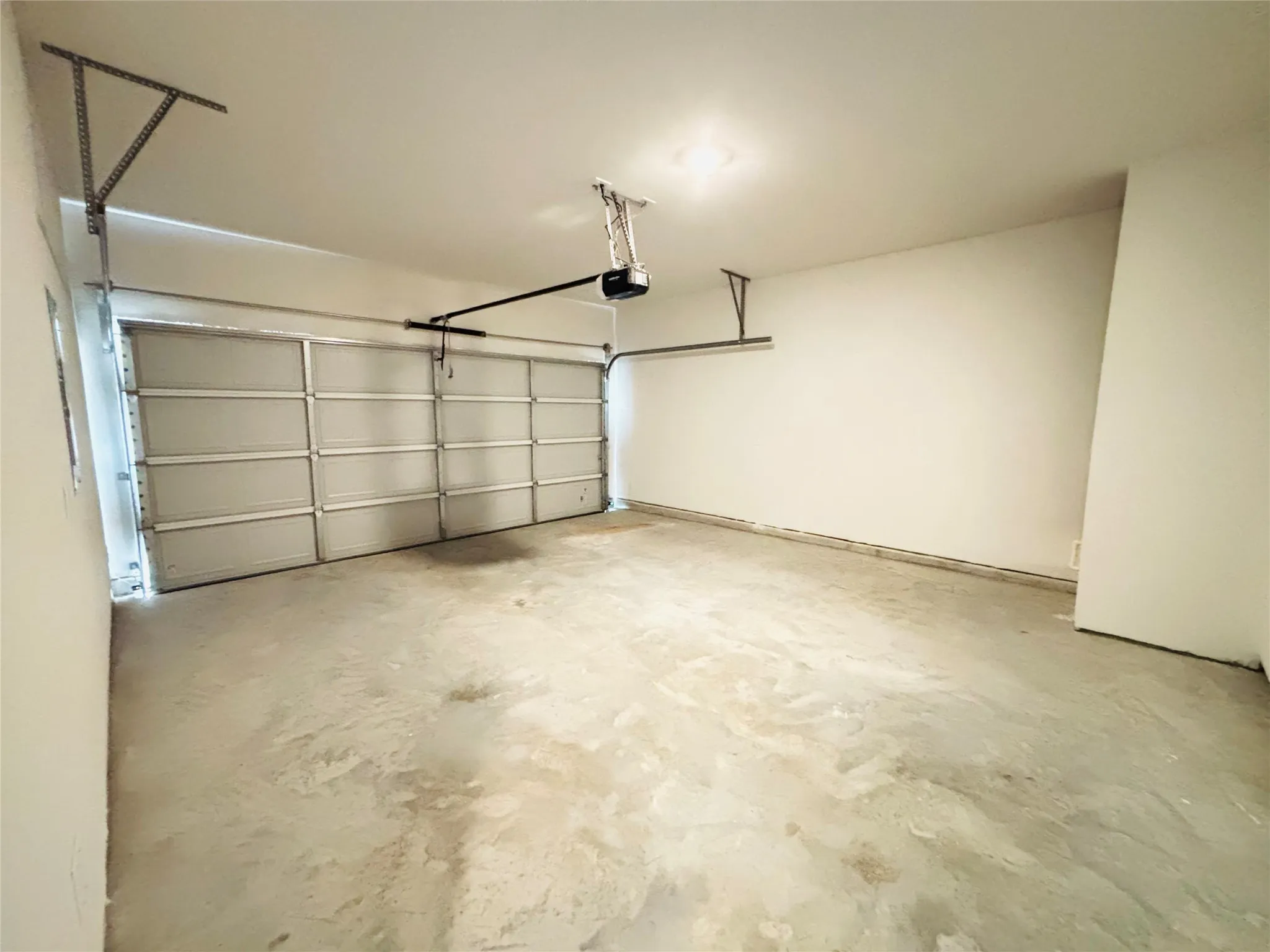 Spacious garage featuring a sectional overhead door, automatic opener, concrete flooring, and an overhead light fixture