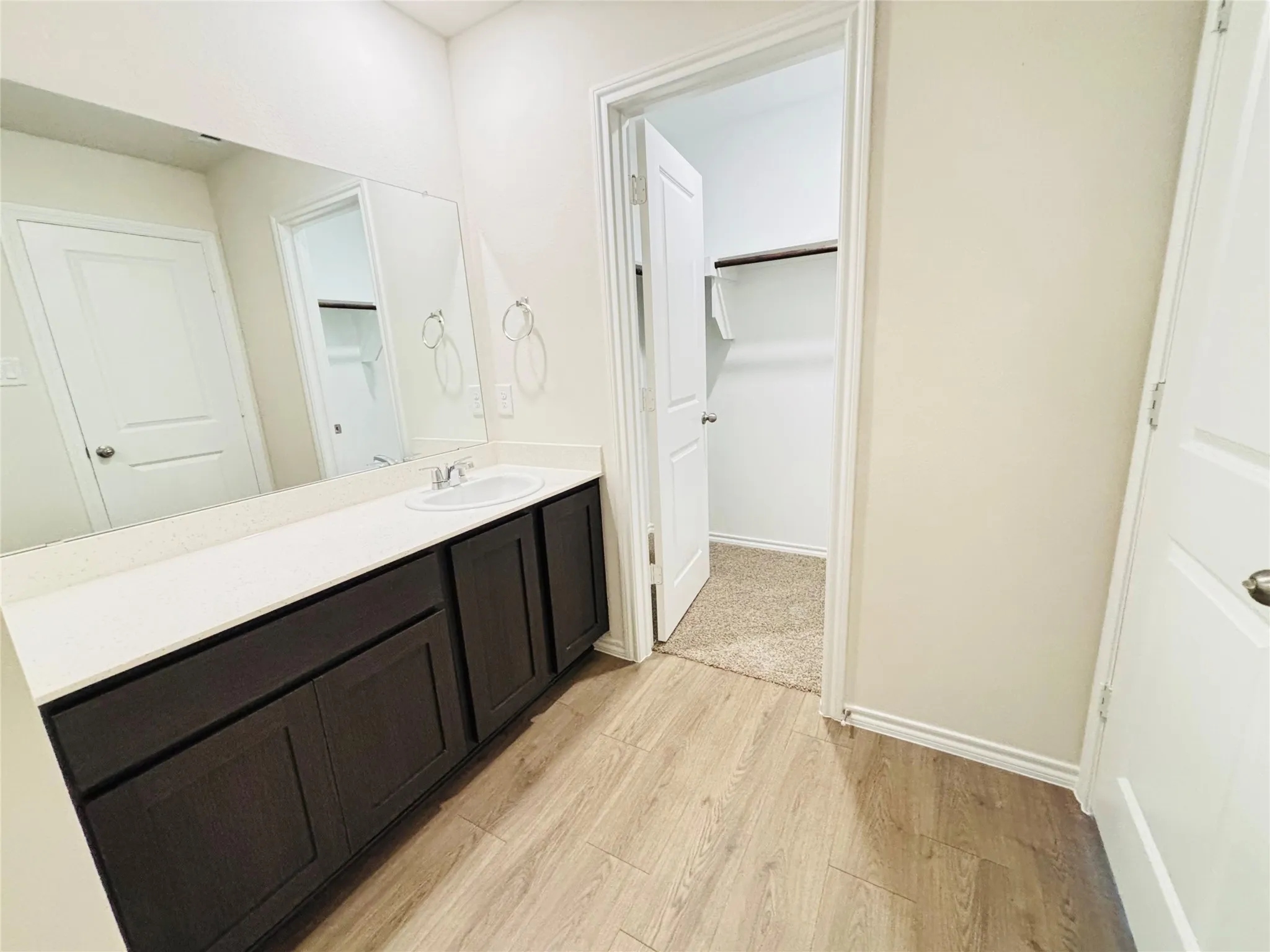 Bathroom vanity featuring a single sink, light countertop, dark cabinetry, and an expansive wall mirror