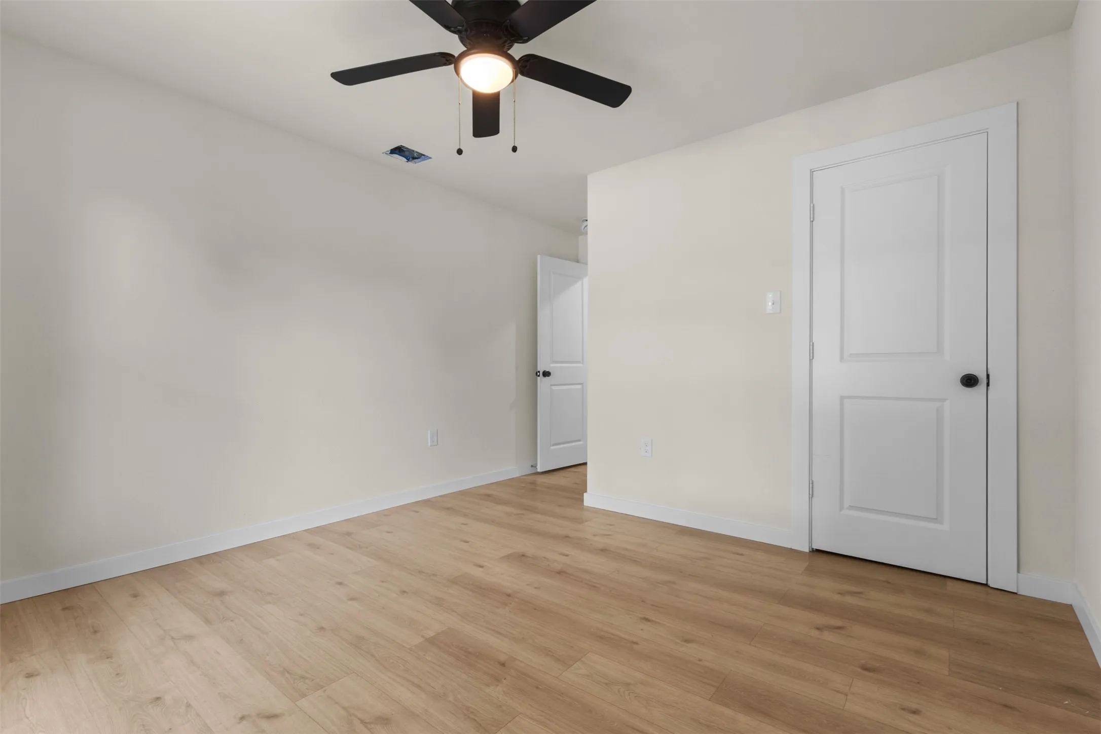 Bedroom featuring wood-finish flooring, light-colored walls, white baseboards, and a black ceiling fan with an integrated light fixture