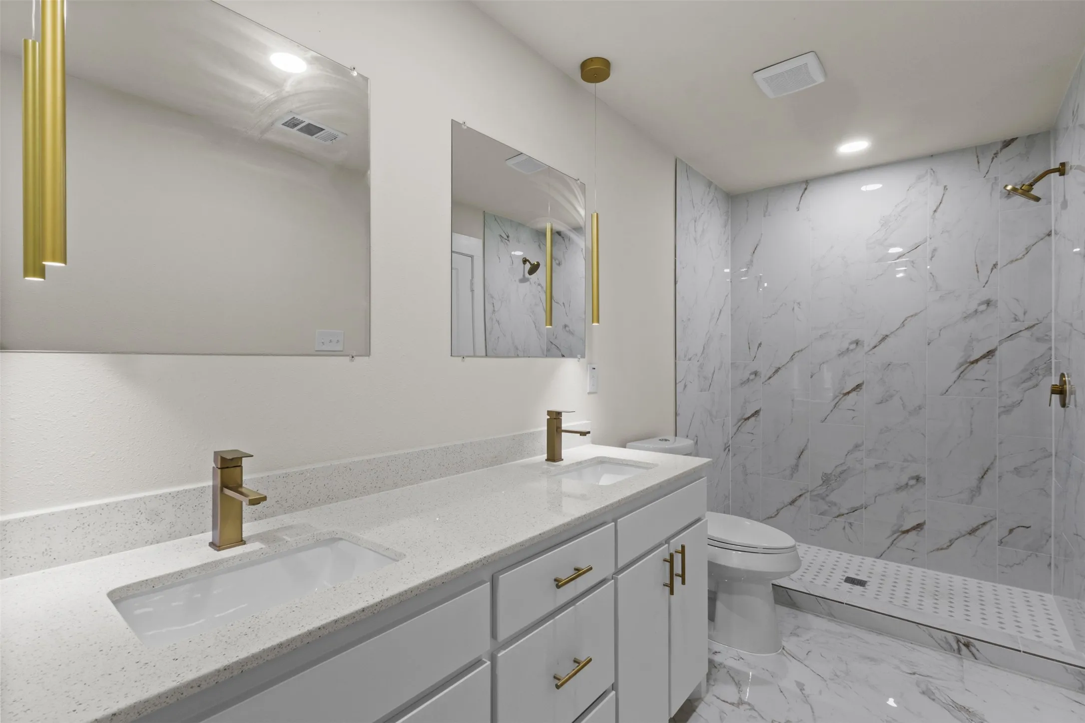 Bathroom featuring a dual vanity with light grey cabinetry and white countertops, under-mount sinks with brass-finish faucets, and two rectangular mirrors