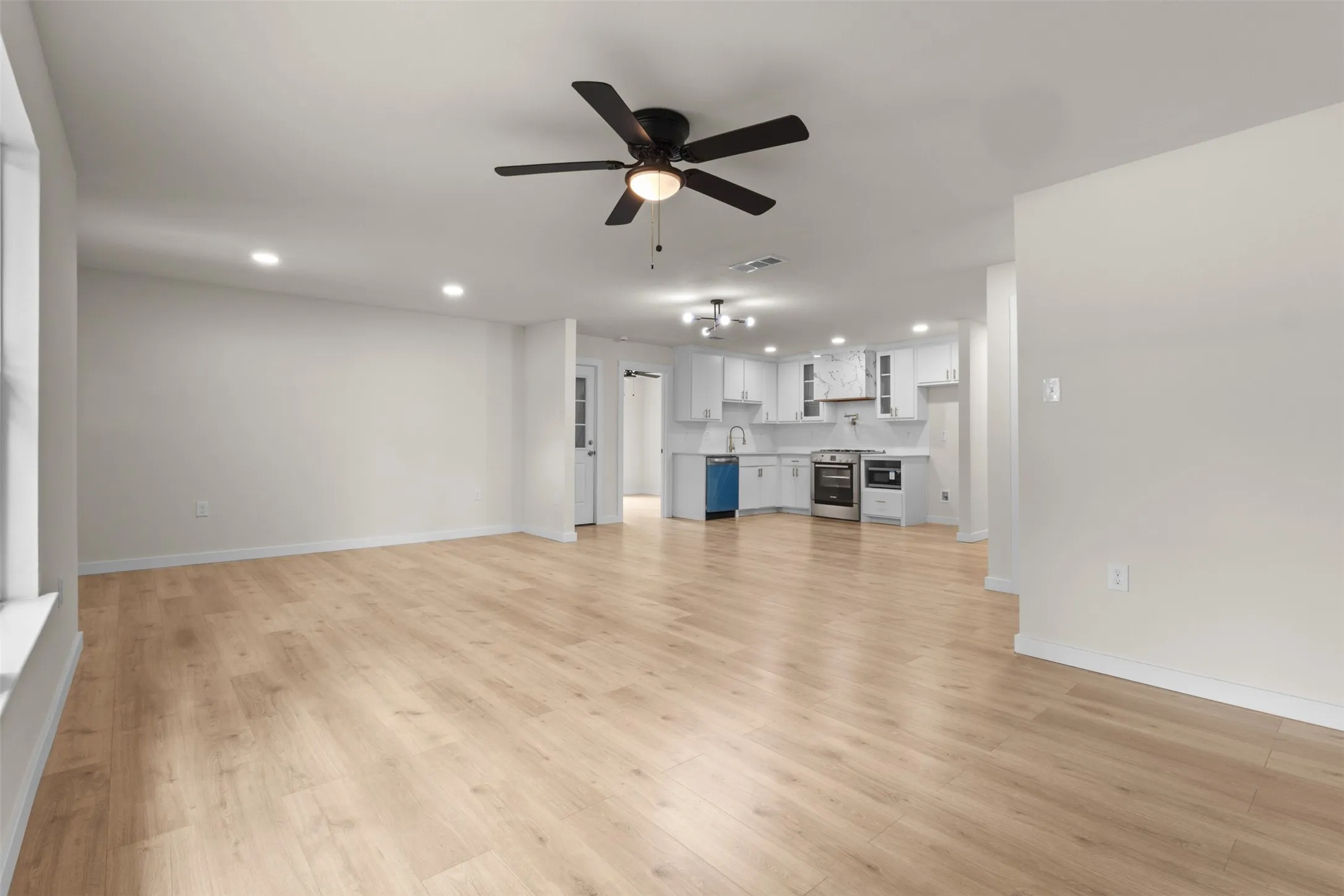 Spacious interior featuring light wood-finish flooring, recessed lighting, and a dark ceiling fan