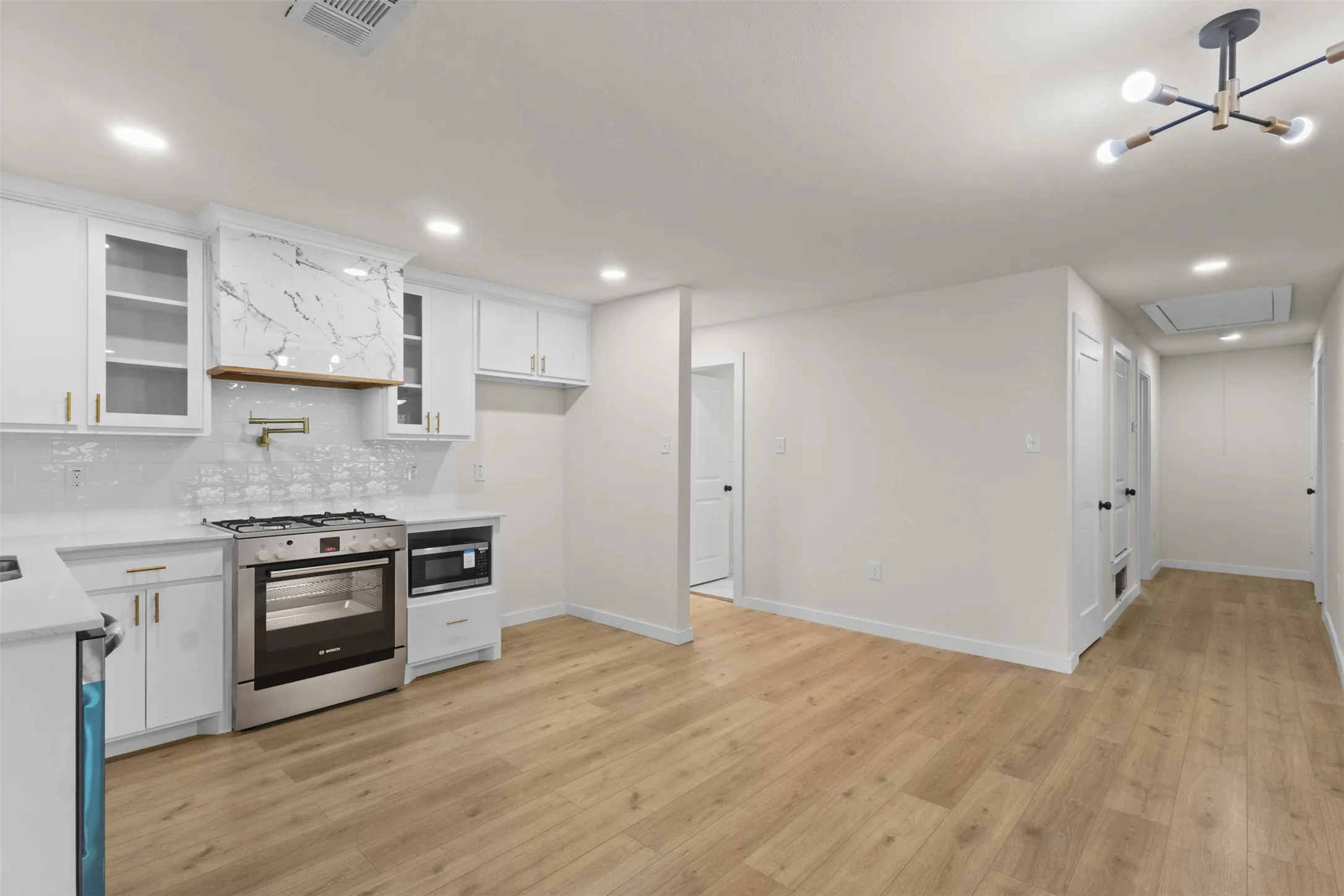 Contemporary kitchen with white cabinetry, stainless steel range and microwave, light wood-finish flooring, and recessed lighting