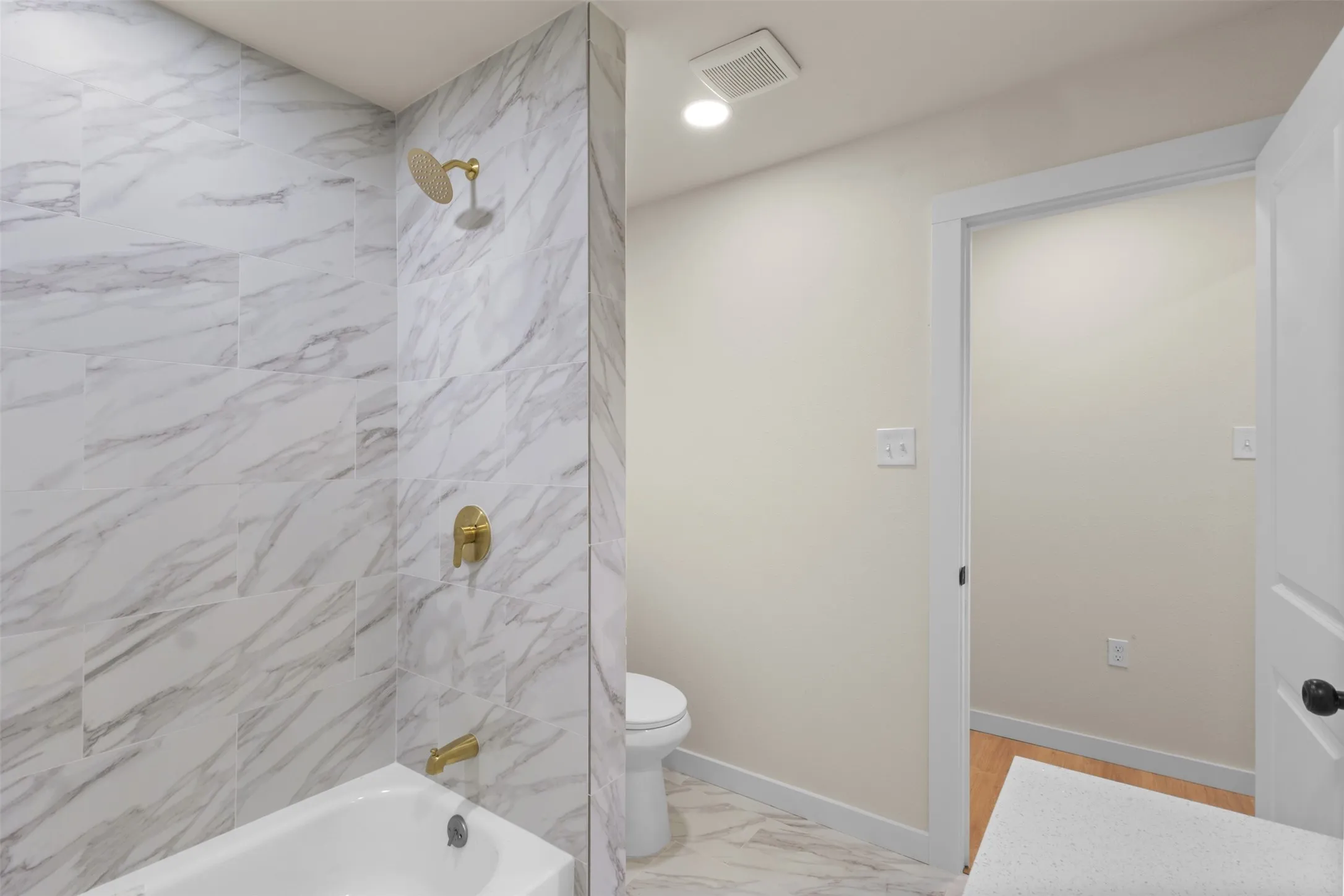 Bathroom featuring a white bathtub, gold-finish shower fixtures, and marble-look wall and floor tiling