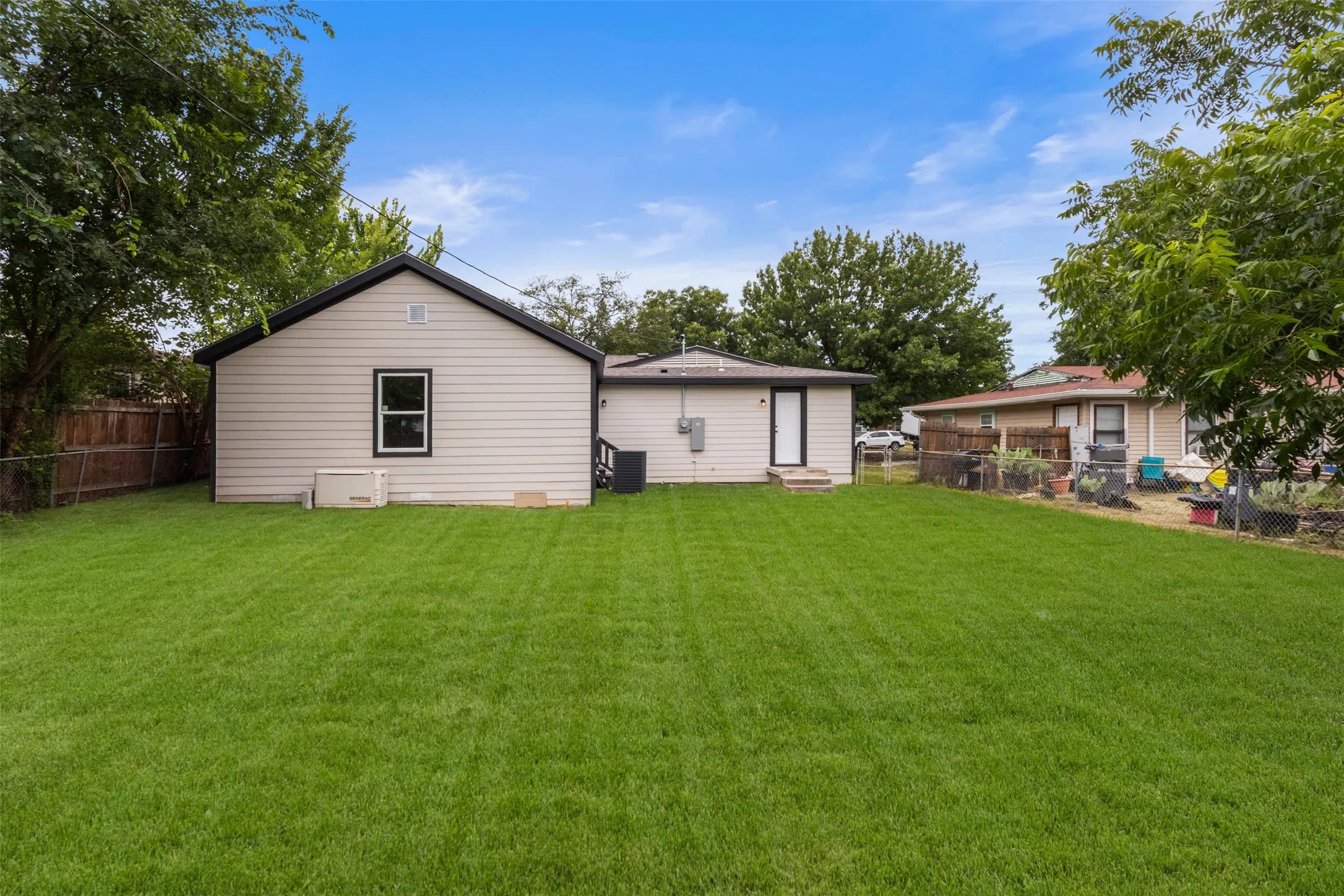 Expansive rear yard featuring a verdant lawn, a detached structure with light-toned siding and a black roofline, and a main dwelling with a rear entry door