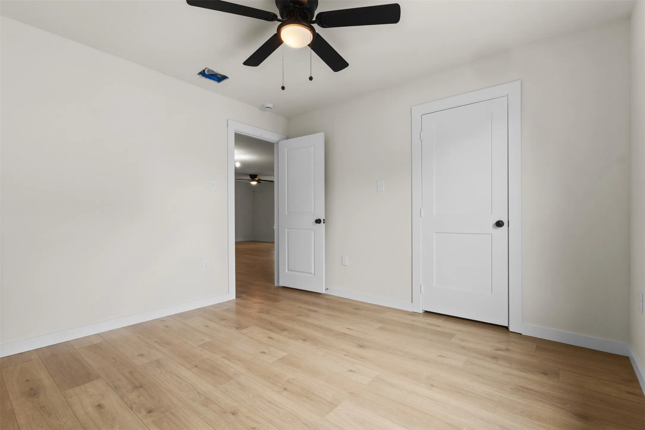 Bright room featuring wood-finish flooring, crisp white walls, and a ceiling fan with integrated lighting