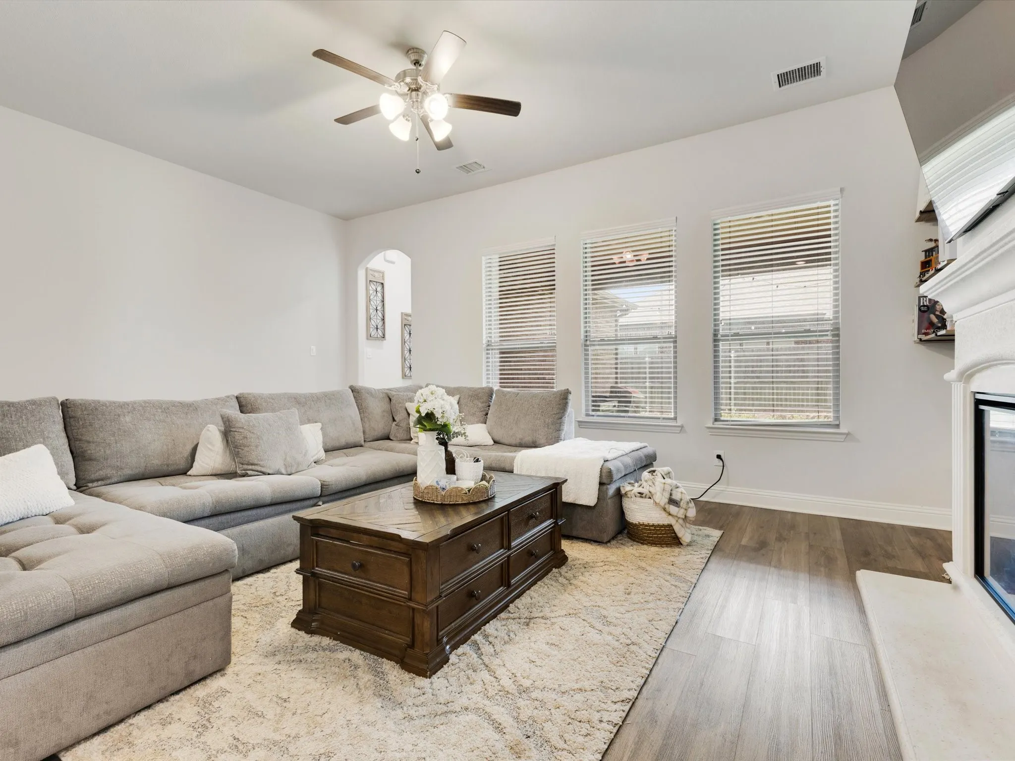 Spacious living area featuring wood-finish flooring, a ceiling fan with integrated lighting, and multiple windows