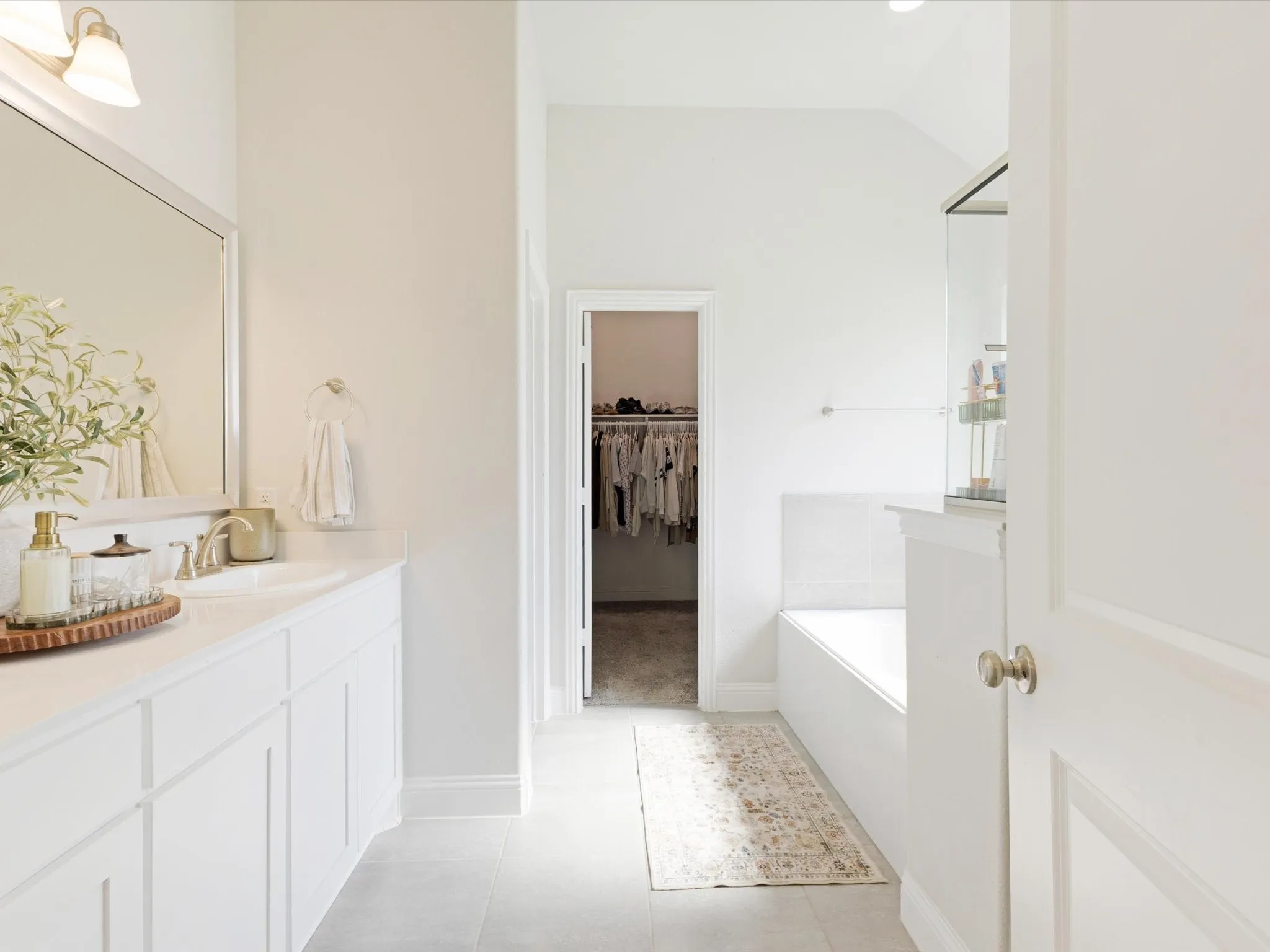 Bathroom featuring a white vanity with extensive storage, a large mirror, and a built-in soaking tub