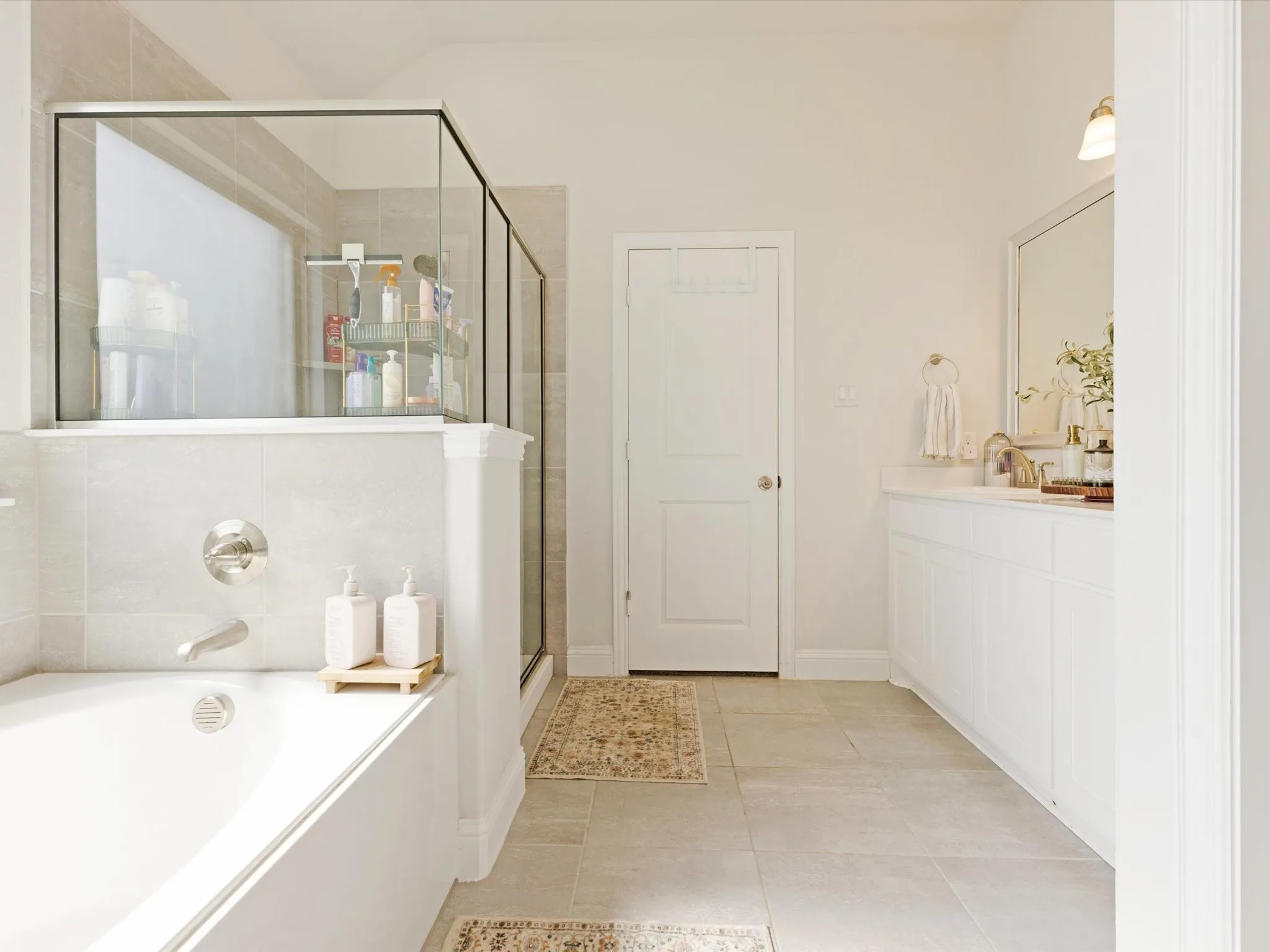 Bathroom featuring a built-in tub, separate glass-enclosed shower, dual vanity with white cabinetry, and large format tile flooring
