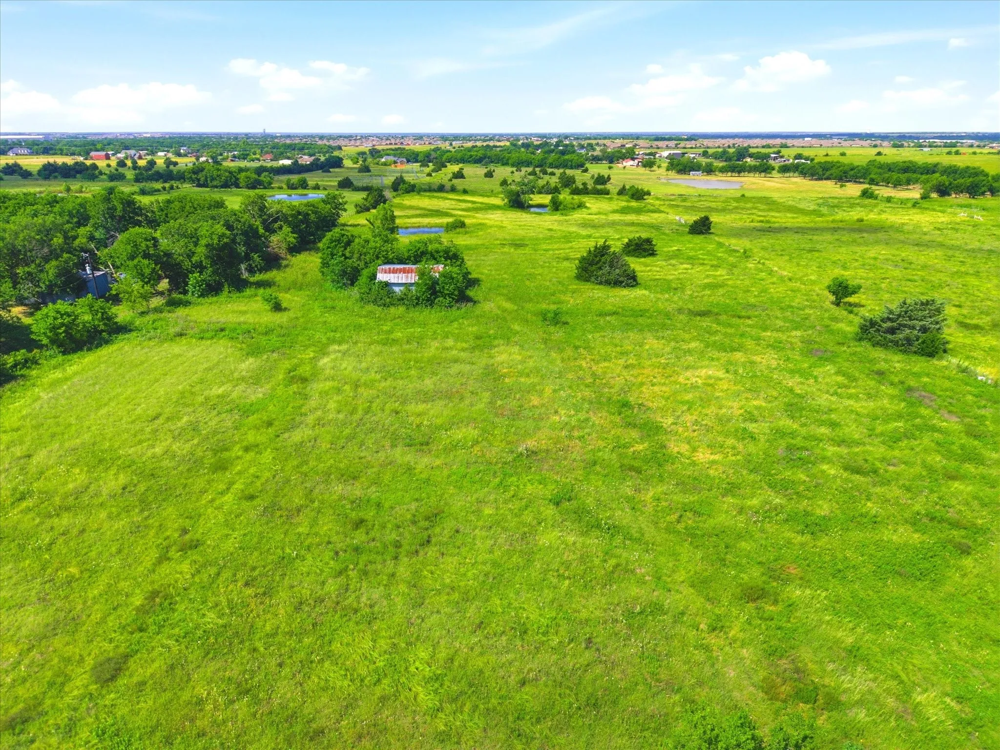 Expansive green acreage featuring scattered trees and a distant building