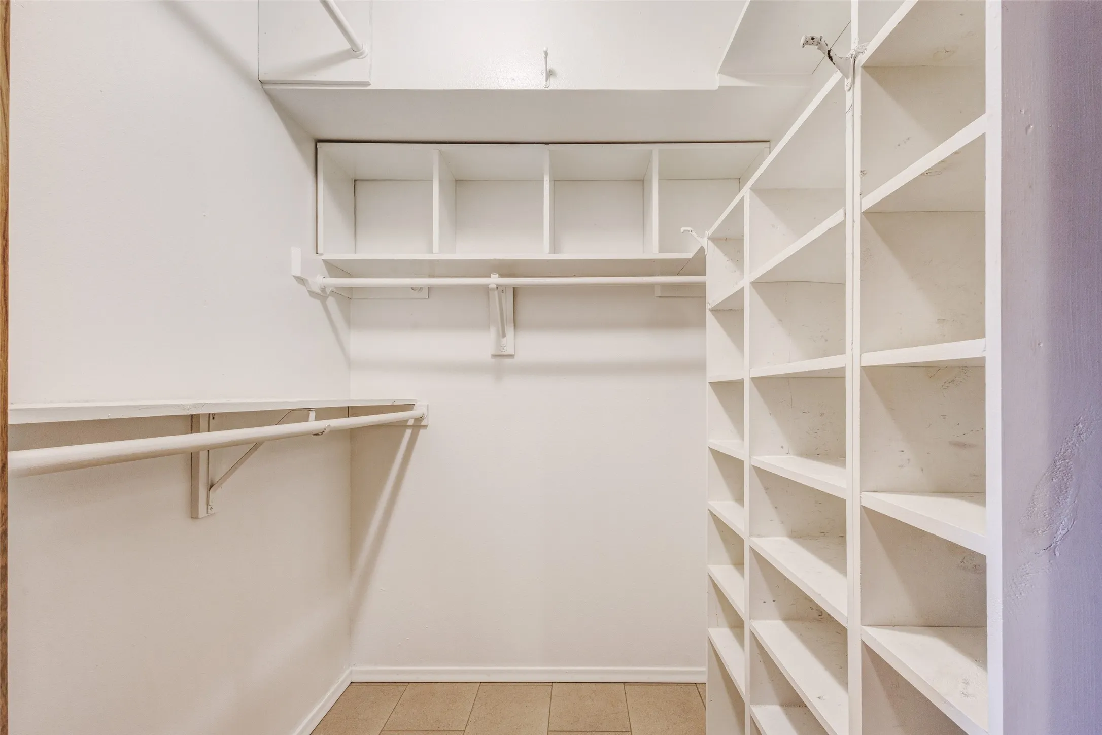 2cWalk-in closets in Primary Bedroom featuring extensive built-in shelving, multiple hanging rods, overhead storage, and tile flooring